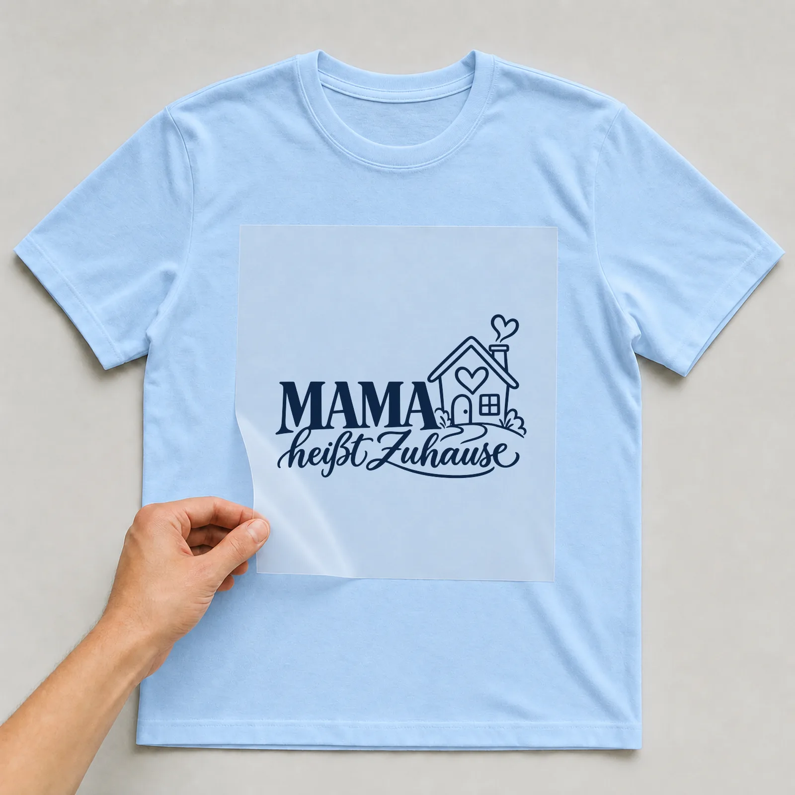 Bügelbild „Mama heißt Zuhause“ auf hellblauem T-Shirt, Folie wird aufgelegt
