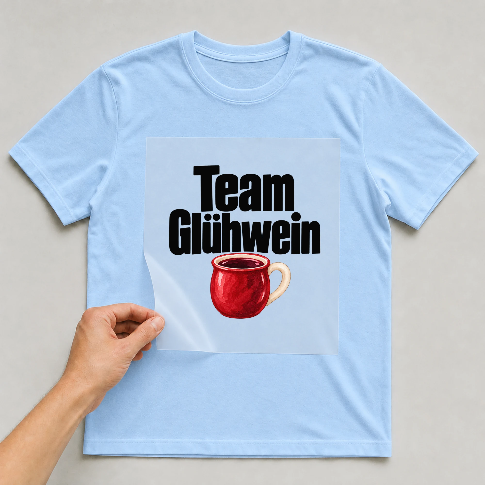 Bügelbild „Team Glühwein“ auf babyblauem T-Shirt, Folie wird aufgelegt