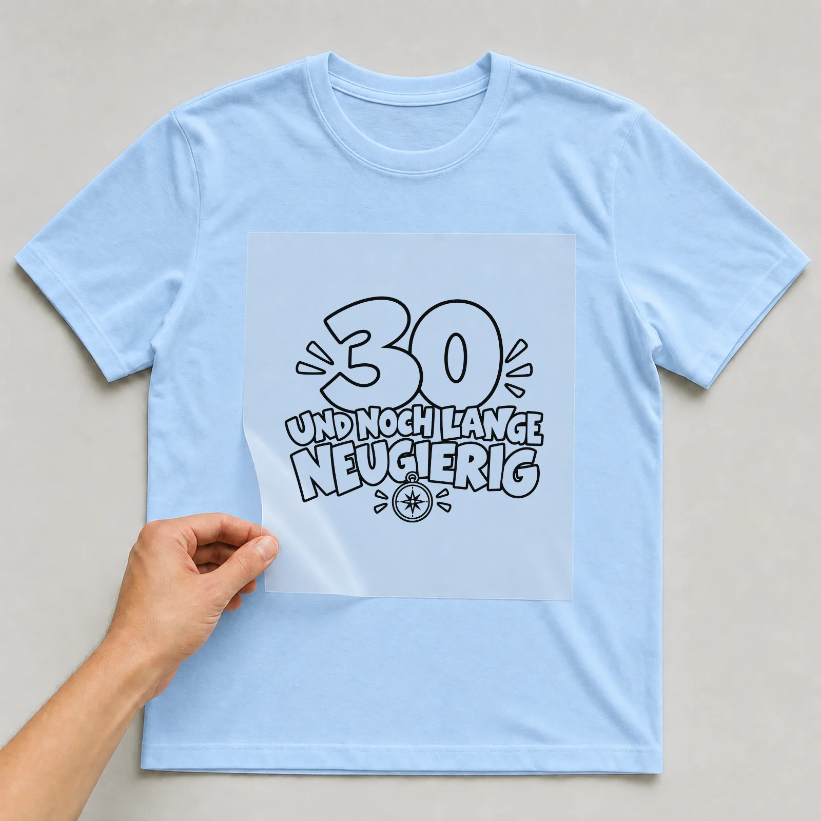 Bügelbild „30 Und noch lange neugierig“ auf hellblauem T-Shirt, Folie wird aufgelegt