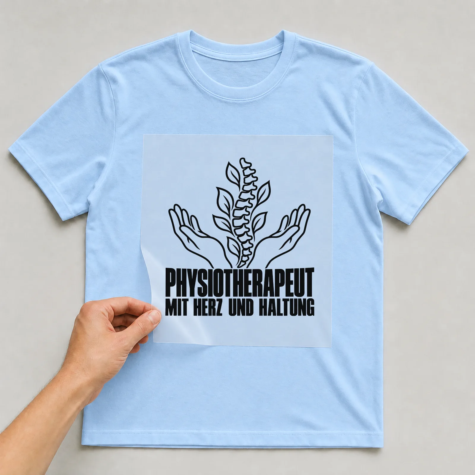 Bügelbild „Physiotherapeut mit Herz und Haltung“ auf hellblauem T-Shirt, Folie wird aufgelegt