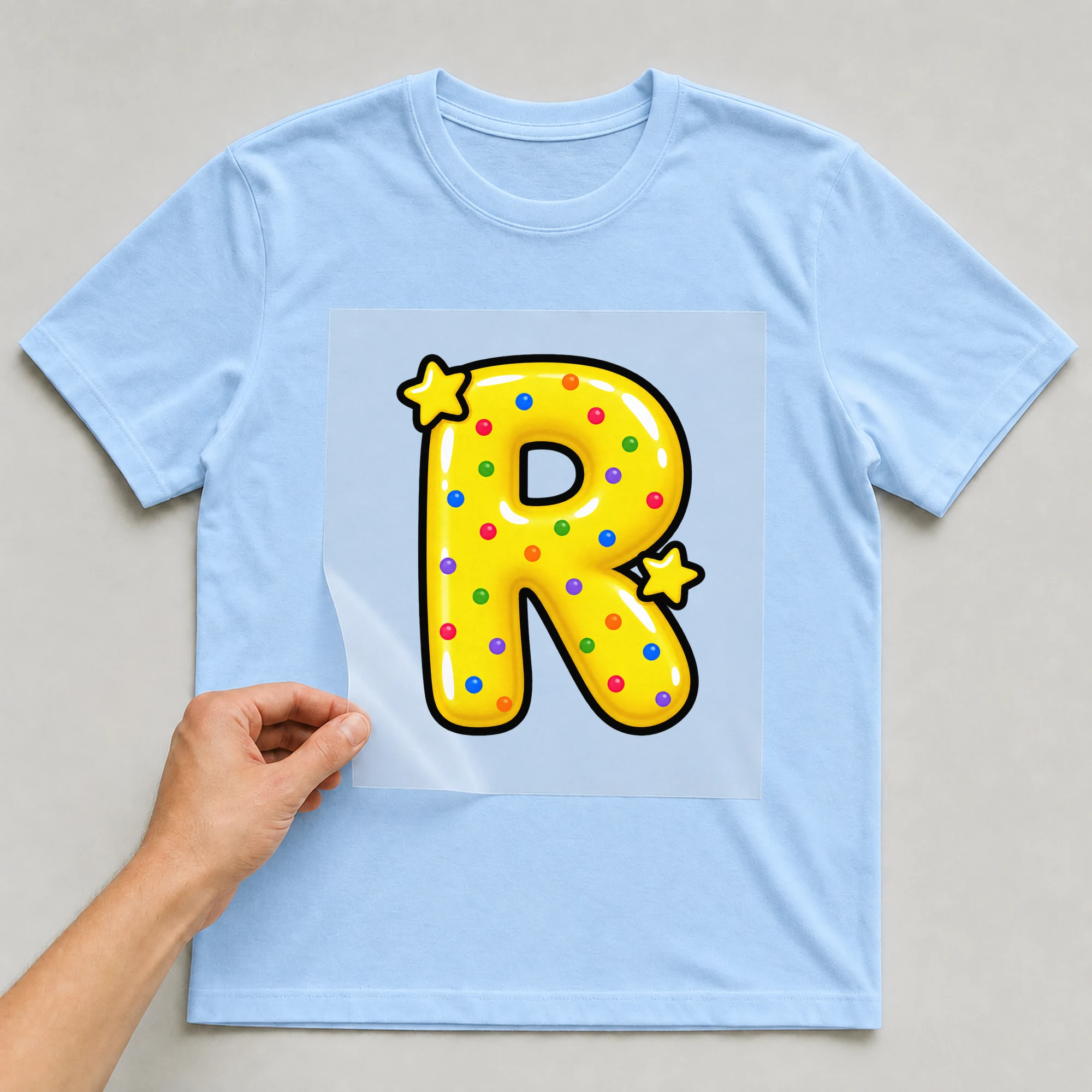 Bügelbild „Buchstabe R im Comic-Ballon-Stil“ auf babyblauem T-Shirt, Folie wird aufgelegt
