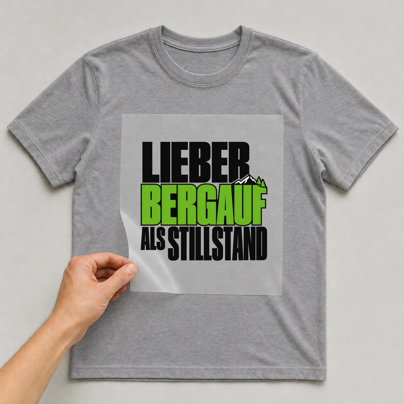 Bügelbild „Lieber bergauf als Stillstand“ auf grauem T-Shirt, Folie wird aufgelegt