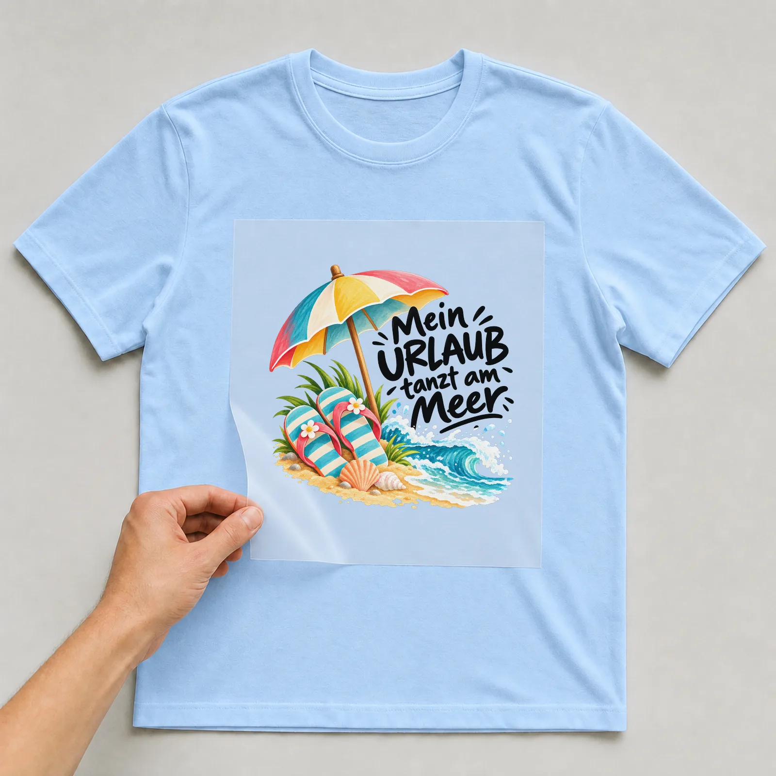 Bügelbild „Mein URLAUB tanzt am Meer“ auf hellblauem T-Shirt, Folie wird aufgelegt