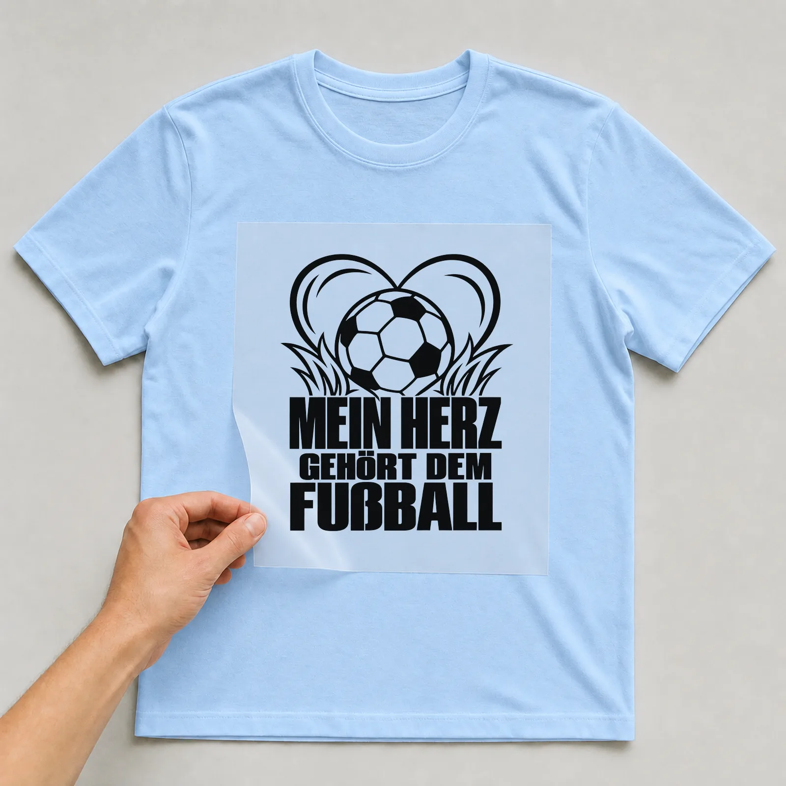 Bügelbild „MEIN HERZ GEHÖRT DEM FUßBALL“ auf hellblauem T-Shirt, Folie wird aufgelegt