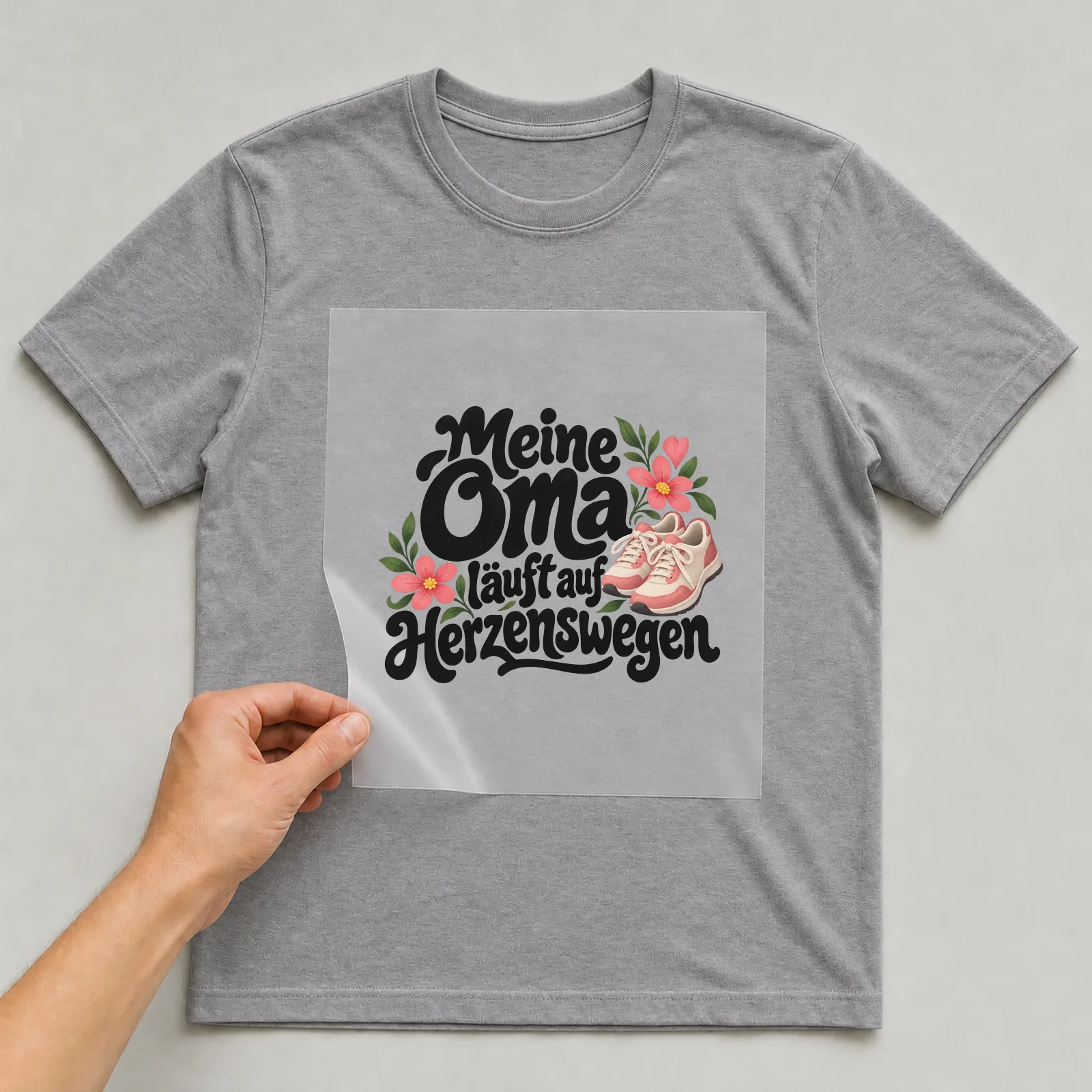 Bügelbild „Meine Oma läuft auf Herzenswegen“ auf grauem T-Shirt, Folie wird aufgelegt