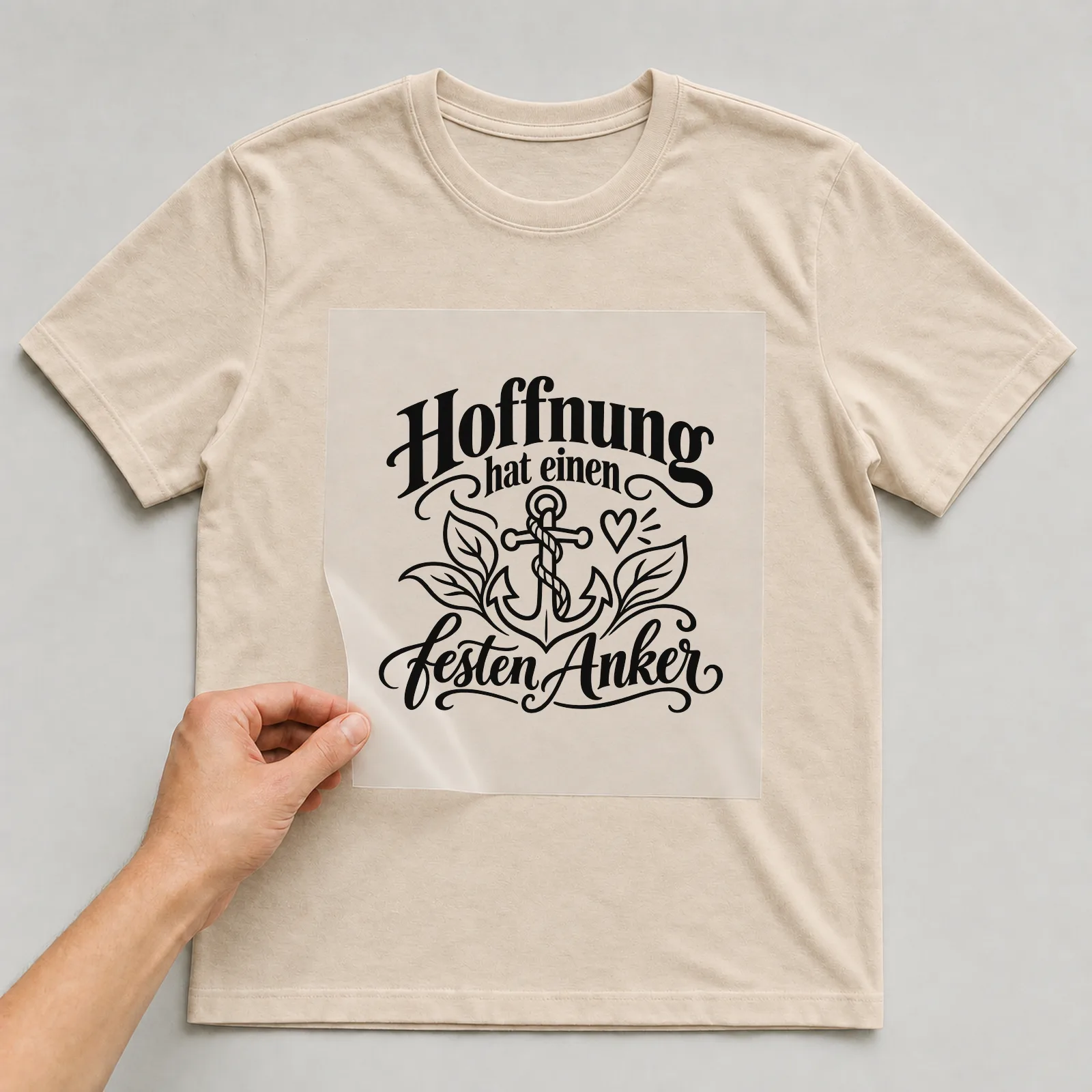 Bügelbild „Hoffnung hat einen festen Anker“ auf beigem T-Shirt, Folie wird aufgelegt