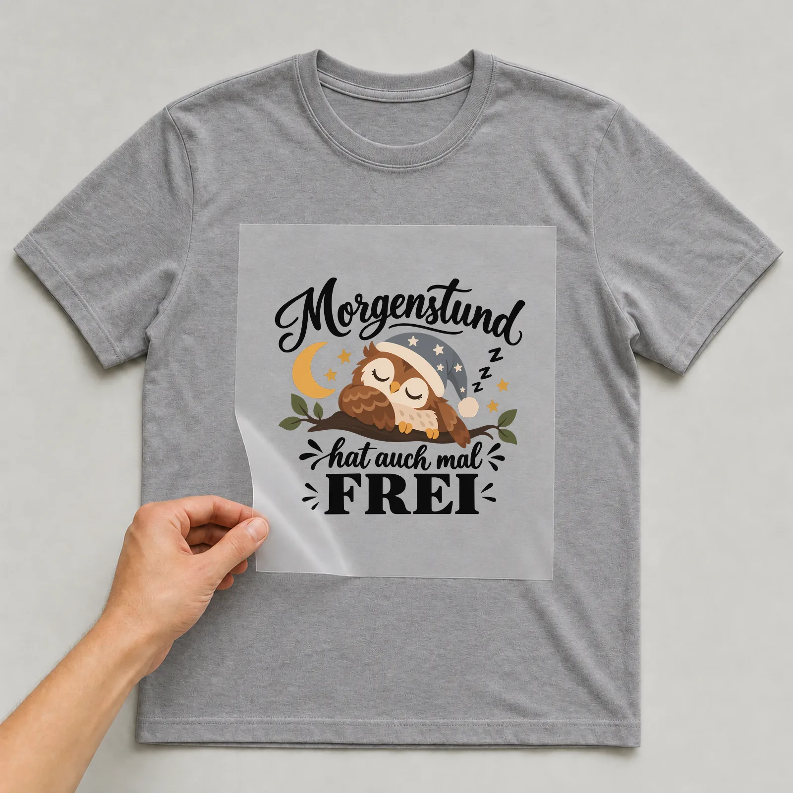 Bügelbild „Morgenstund hat auch mal frei“ auf grauem T-Shirt, Folie wird aufgelegt