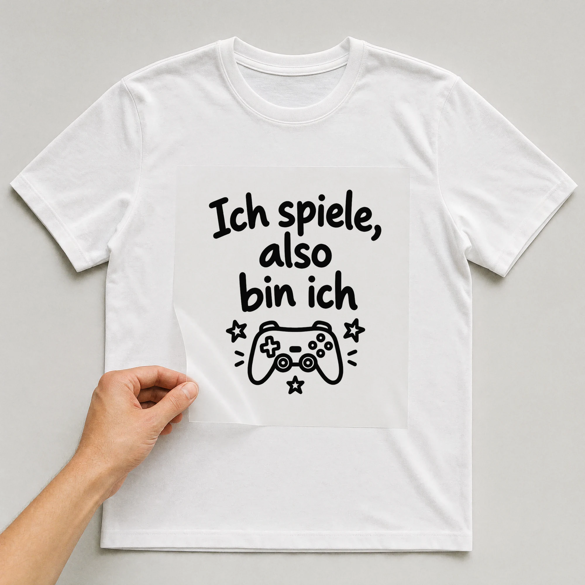 Bügelbild „Ich spiele, also bin ich“ auf weißem T-Shirt, Folie wird aufgelegt