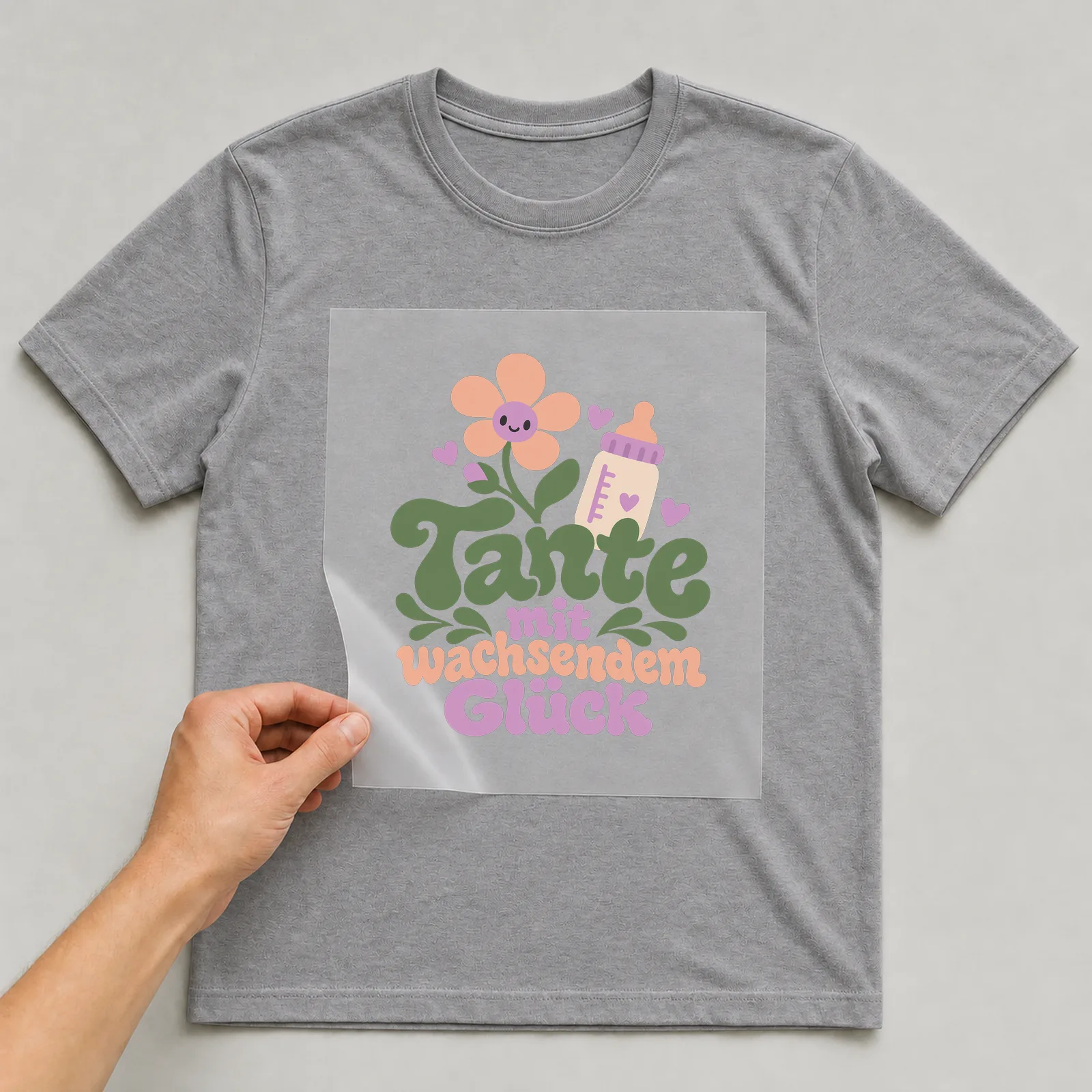 Bügelbild „Tante mit wachsendem Glück“ auf grauem T-Shirt, Folie wird aufgelegt