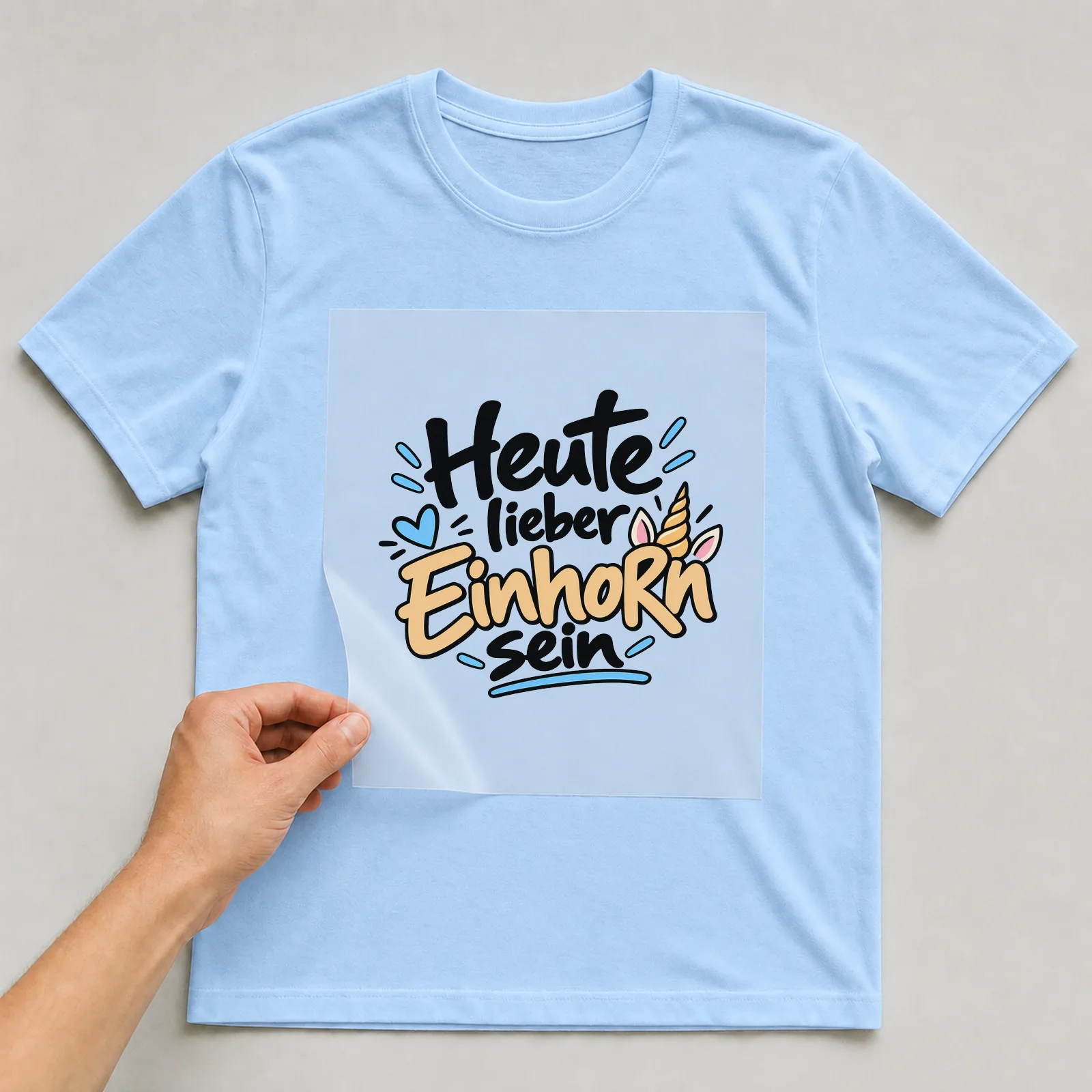 Bügelbild „Heute lieber Einhorn sein“ auf hellblauem T-Shirt, Folie wird aufgelegt
