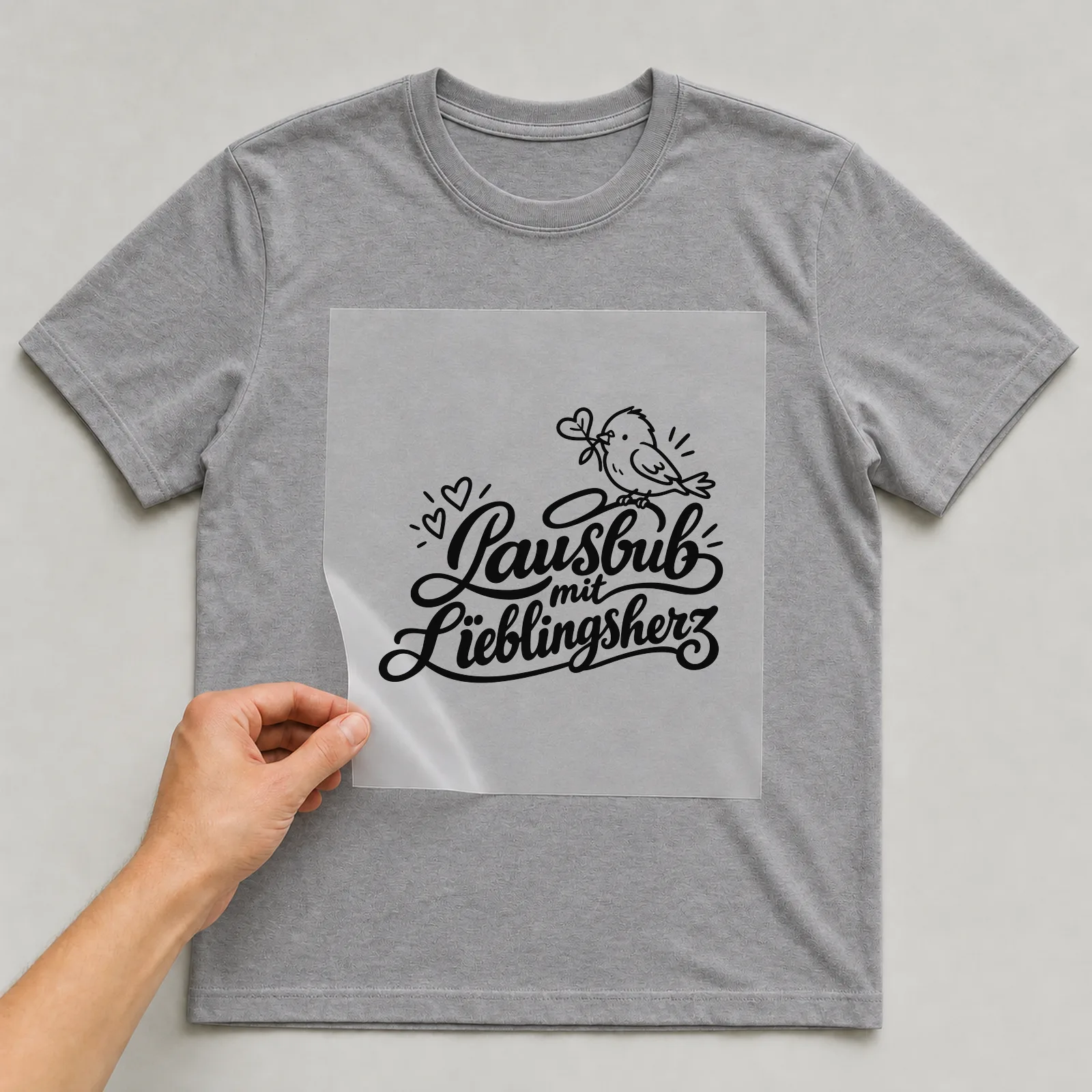 Bügelbild „Lausbub mit Lieblingsherz“ auf grauem T-Shirt, Folie wird aufgelegt