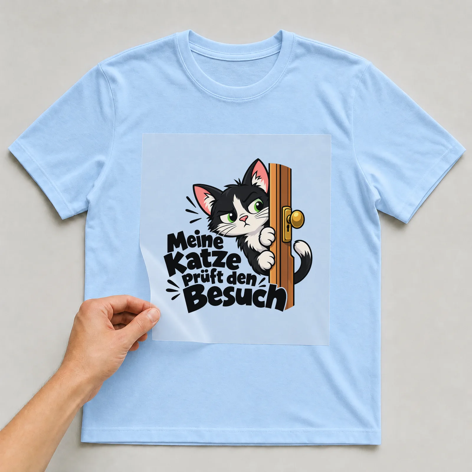 Bügelbild „Meine Katze prüft den Besuch“ auf hellblauem T-Shirt, Folie wird aufgelegt