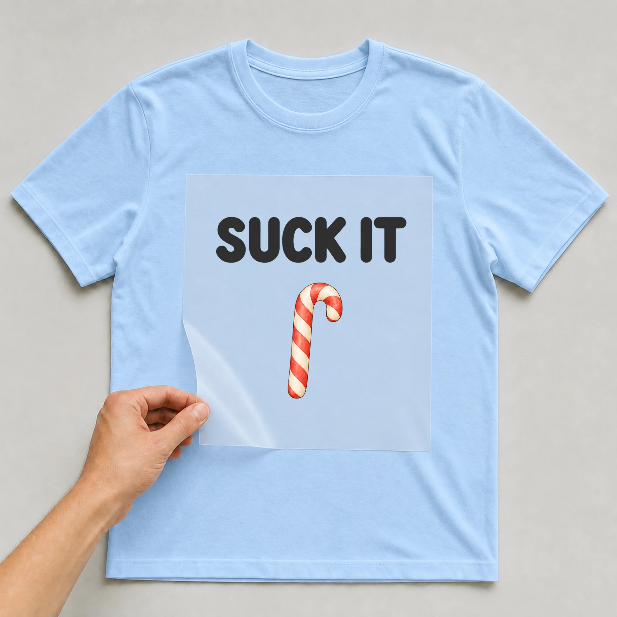 Bügelbild „SUCK IT“ auf babyblauem T-Shirt, Folie wird aufgelegt