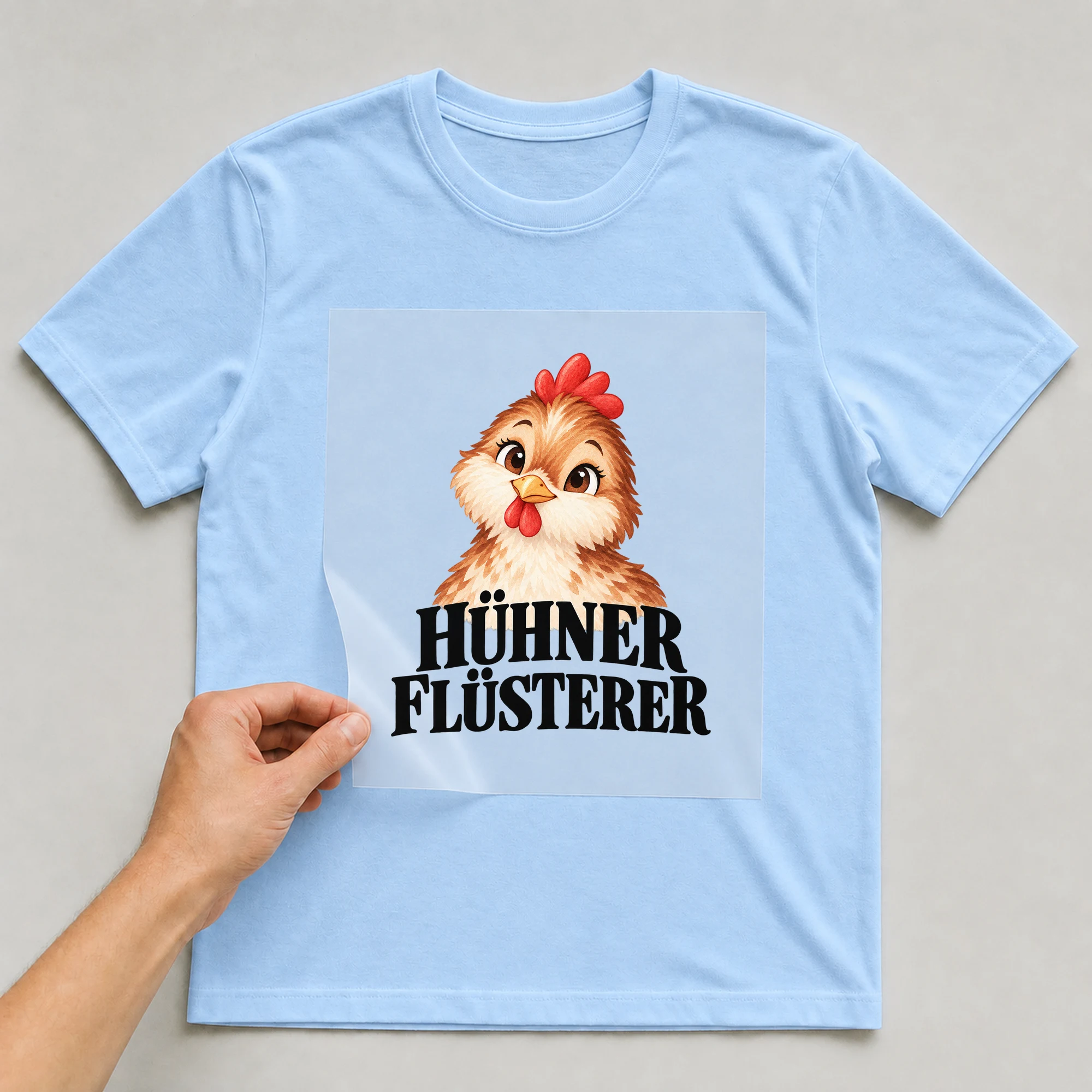Bügelbild „Hühner Flüsterer“ auf babyblauem T-Shirt, Folie wird aufgelegt
