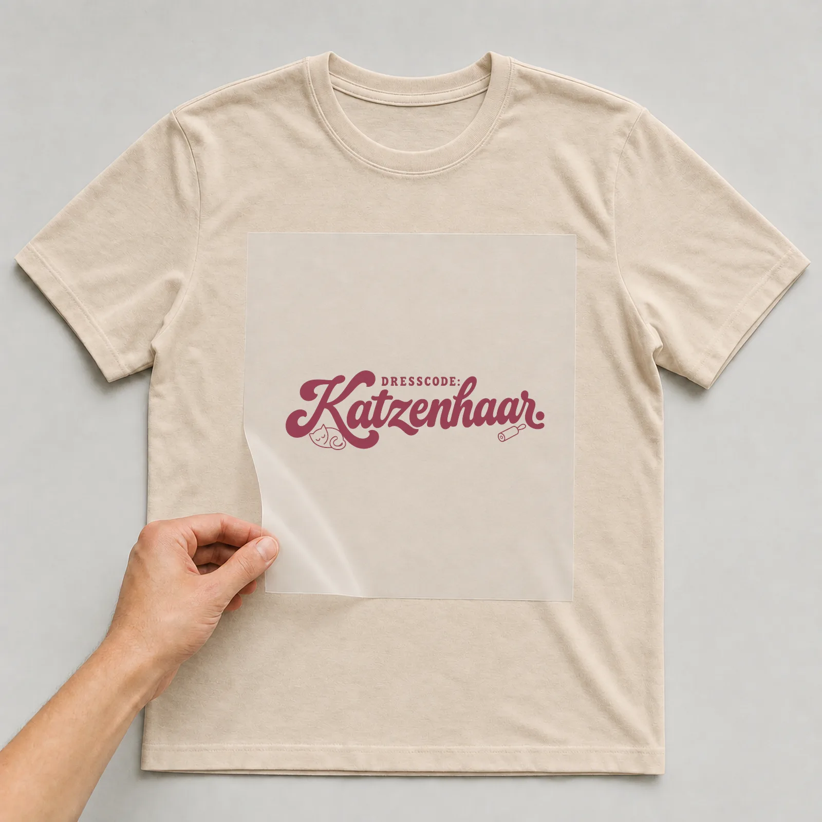 Bügelbild „DRESSCODE: Katzenhaar“ (Schrift Konturen, Nr. 3) auf beigem T-Shirt, Folie wird aufgelegt