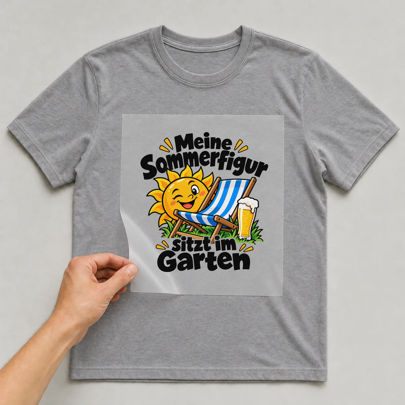 Bügelbild „Meine Sommerfigur sitzt im Garten“ auf grauem T-Shirt, Folie wird aufgelegt