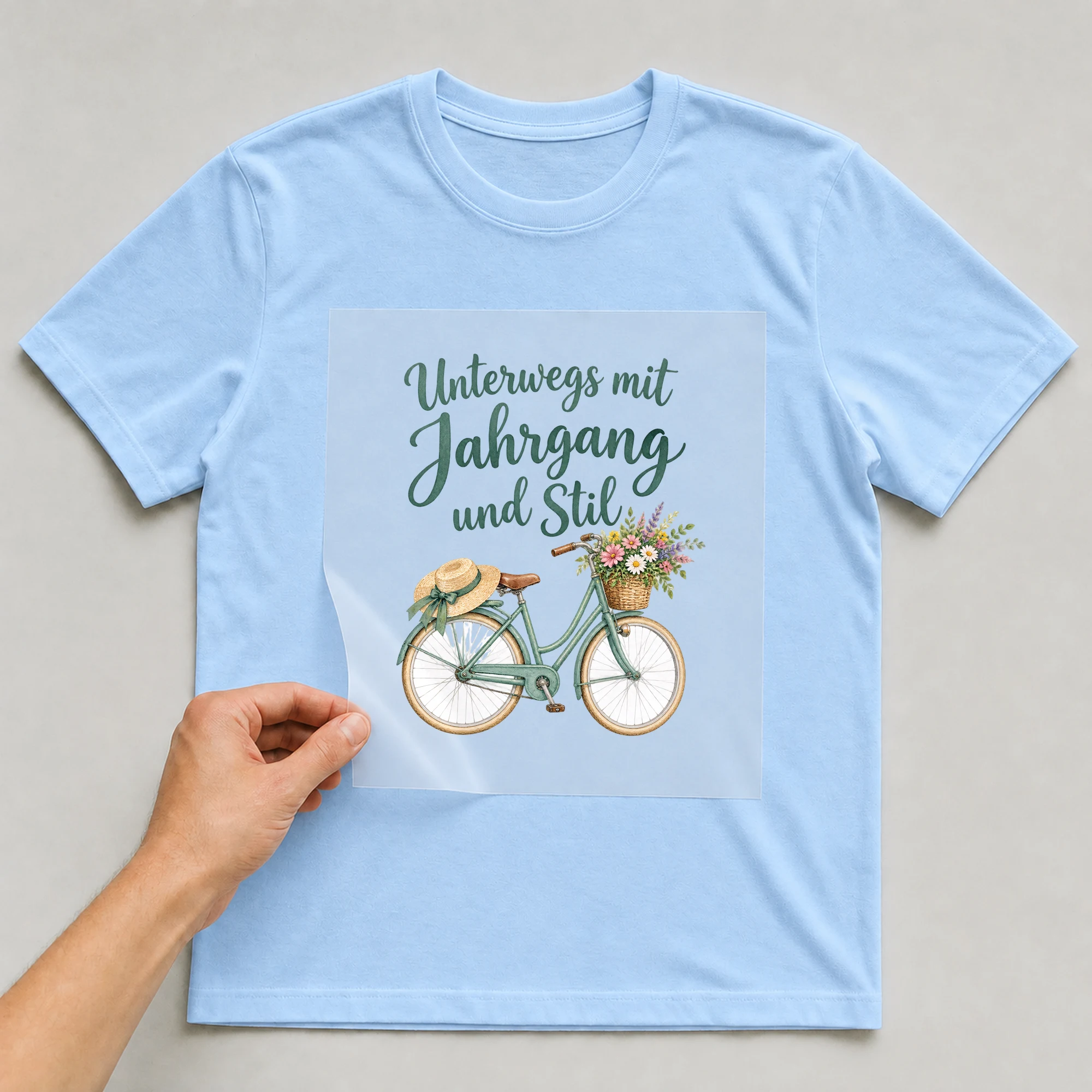 Bügelbild „Unterwegs mit Jahrgang und Stil“ auf babyblauem T-Shirt, Folie wird aufgelegt