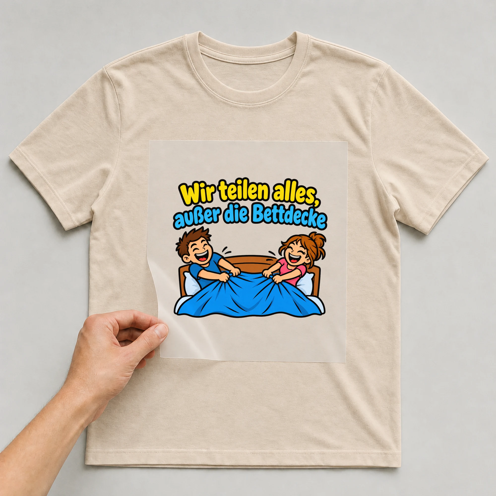 Bügelbild „Wir teilen alles, außer die Bettdecke“ auf beigem T-Shirt, Folie wird aufgelegt