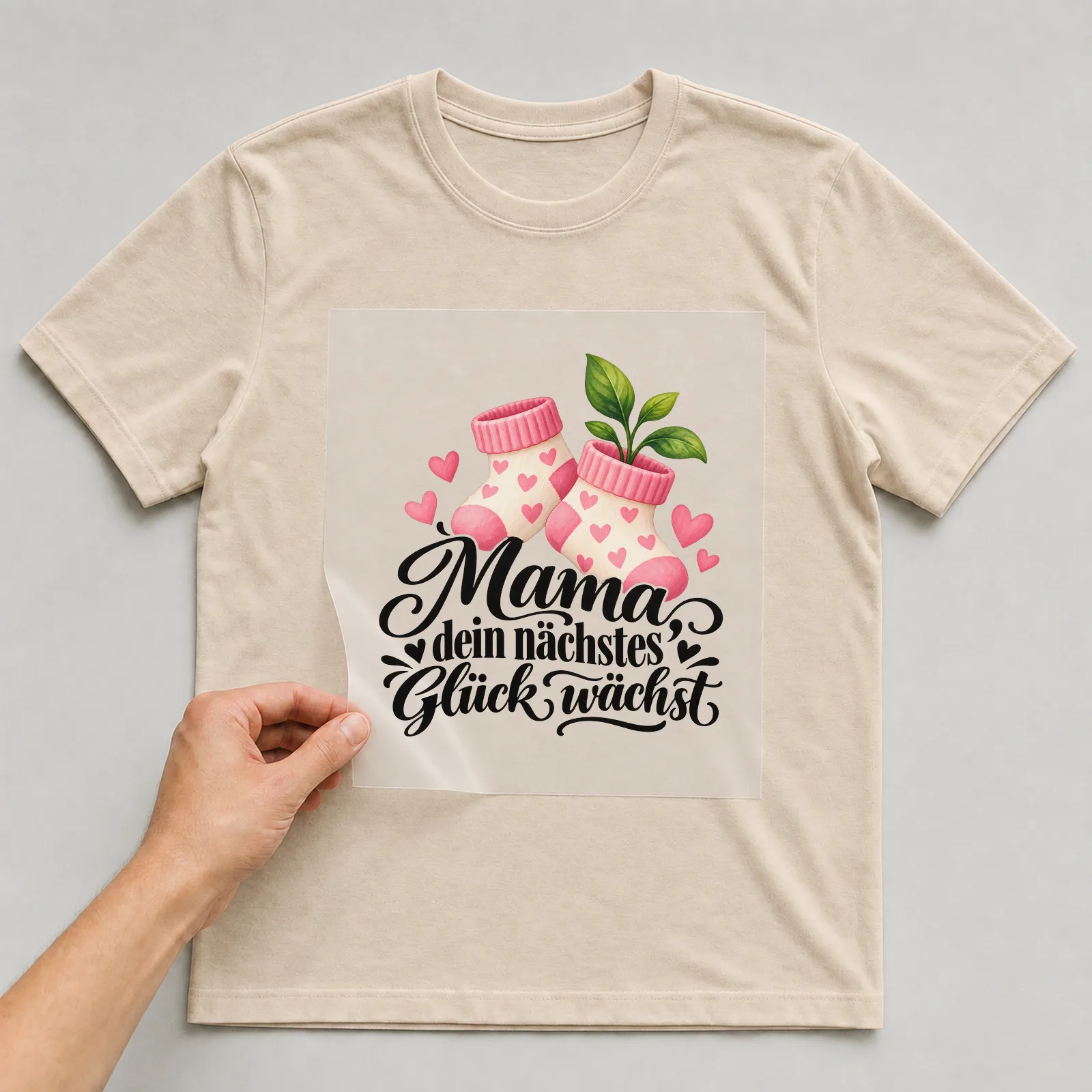 Bügelbild „Mama dein nächstes Glück wächst“ auf beigem T-Shirt, Folie wird aufgelegt
