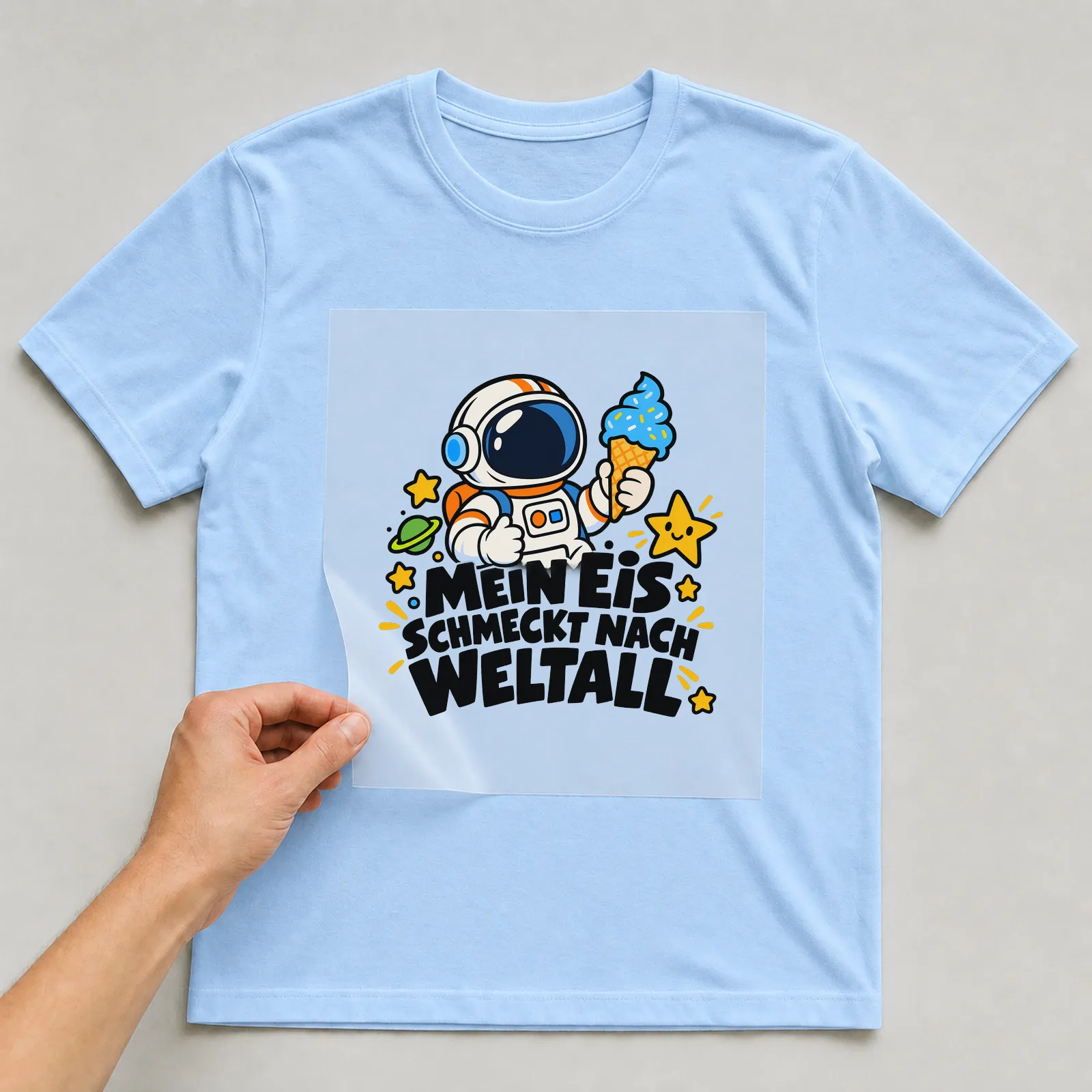 Bügelbild „Mein Eis schmeckt nach Weltall“ auf hellblauem T-Shirt, Folie wird aufgelegt