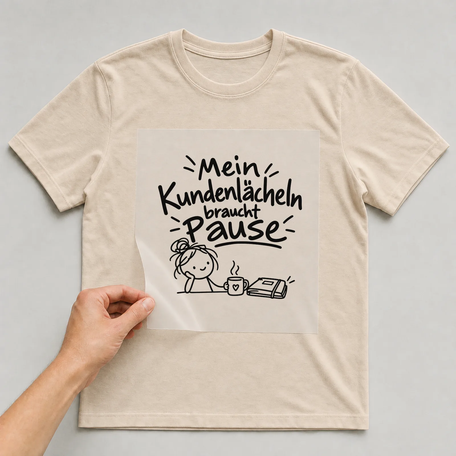 Bügelbild „Mein Kundenlächeln braucht Pause“ auf beigem T-Shirt, Folie wird aufgelegt