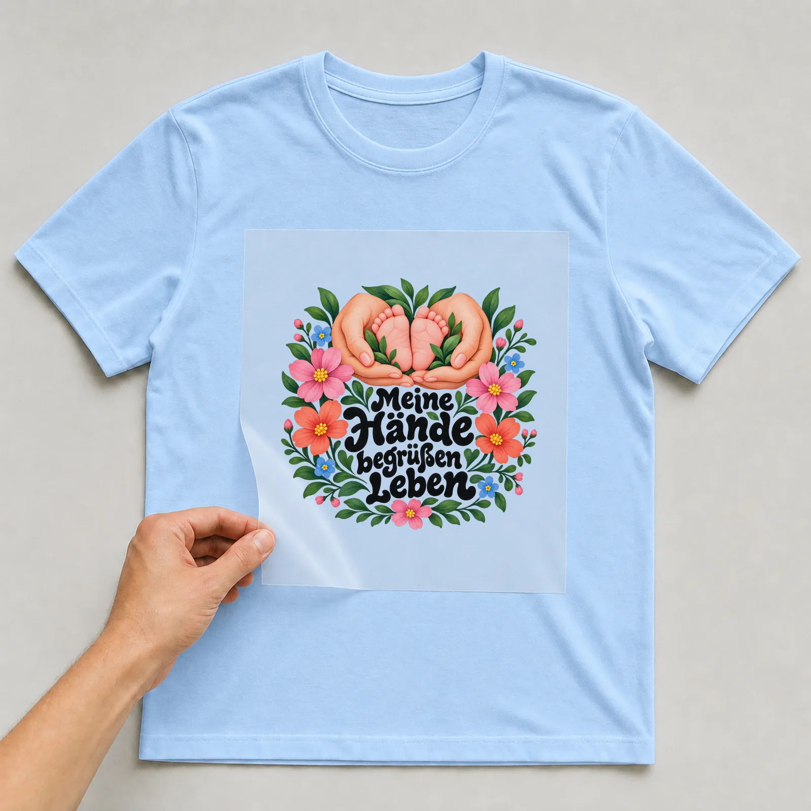 Bügelbild „Meine Hände begrüßen Leben“ auf hellblauem T-Shirt, Folie wird aufgelegt