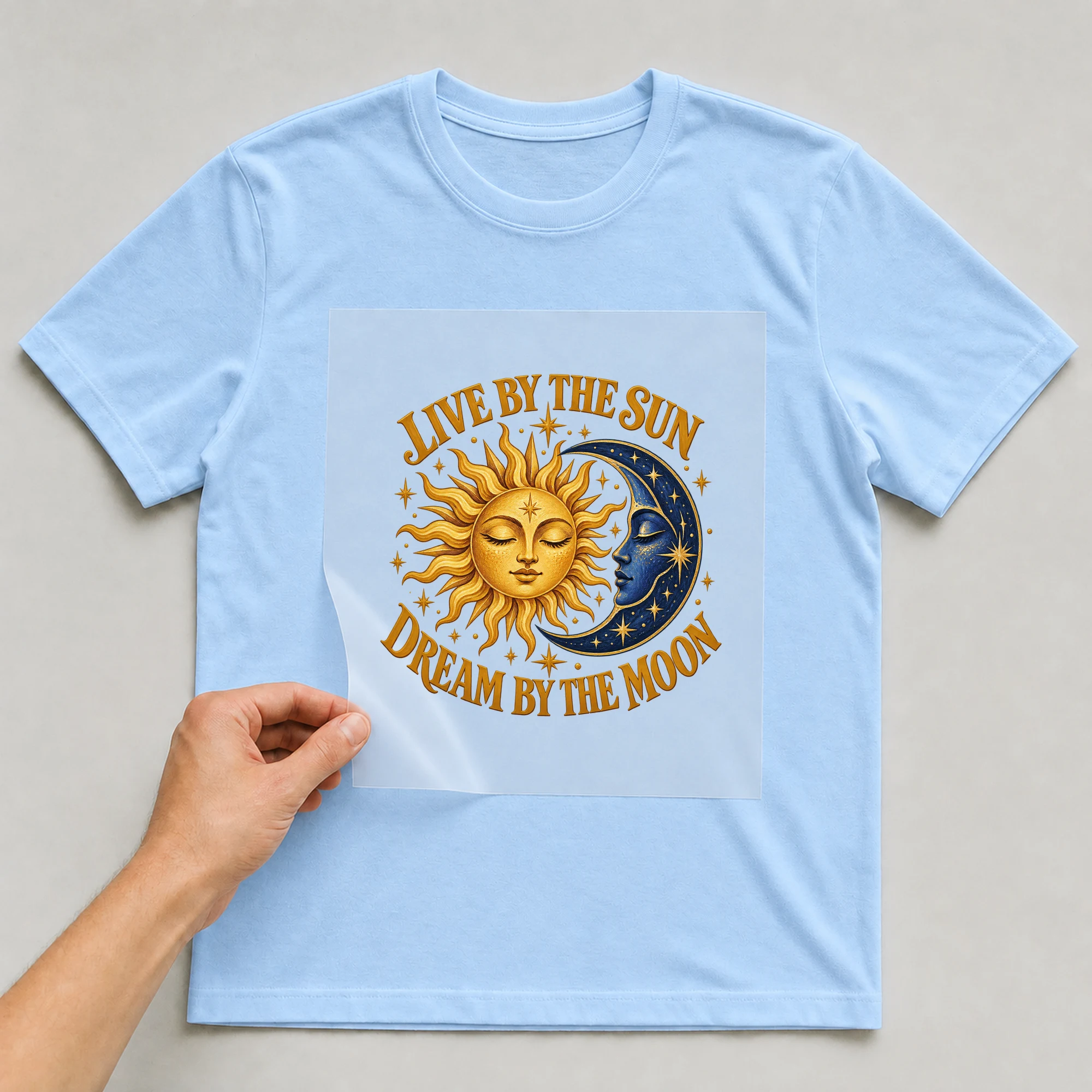 Bügelbild „Live By The Sun Dream By The Moon“ auf babyblauem T-Shirt, Folie wird aufgelegt