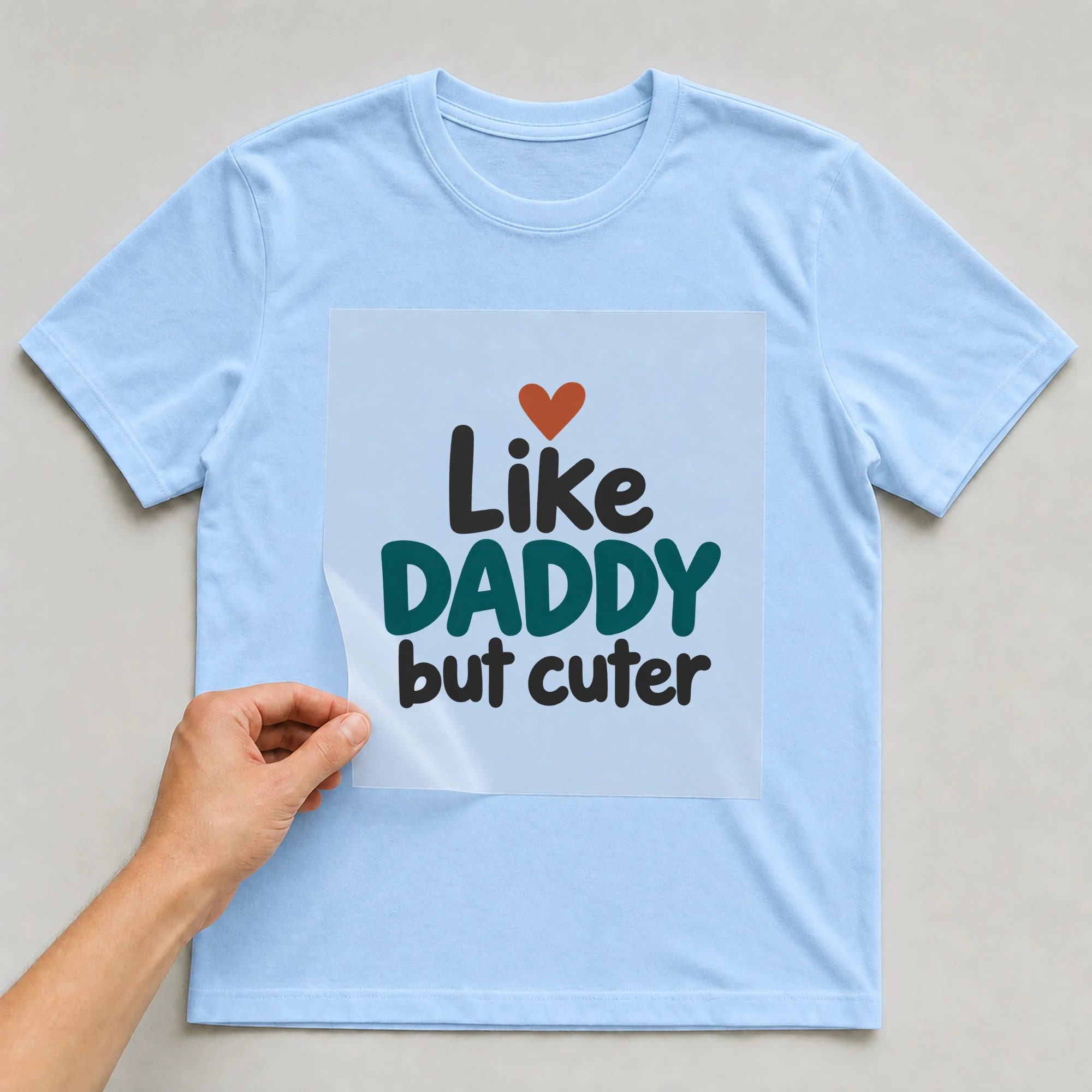 Bügelbild „Like DADDY but cuter“ auf babyblauem T-Shirt, Folie wird aufgelegt