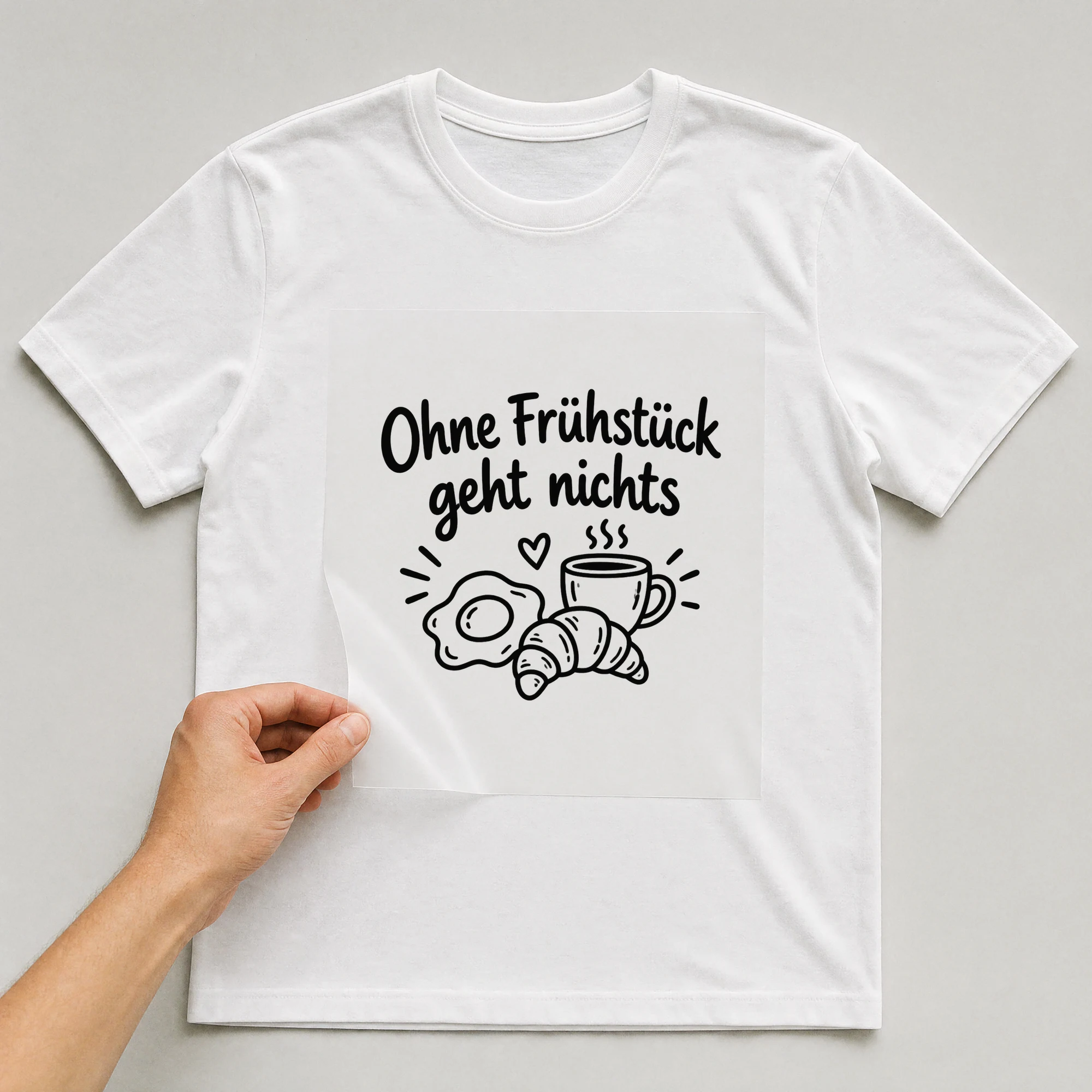 Bügelbild „Ohne Frühstück geht nichts“ auf weißem T-Shirt, Folie wird aufgelegt