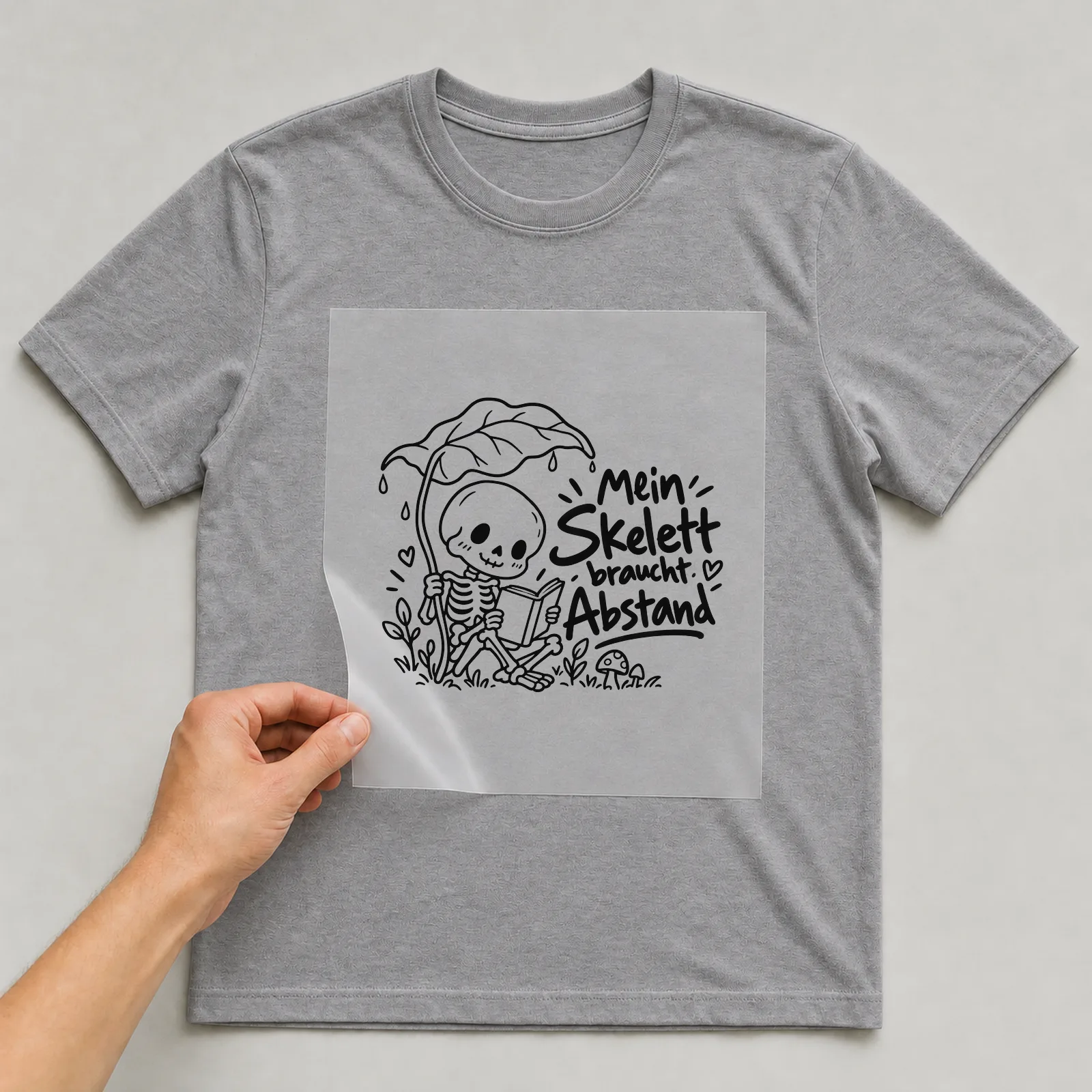 Bügelbild „Mein Skelett braucht Abstand“ auf grauem T-Shirt, Folie wird aufgelegt