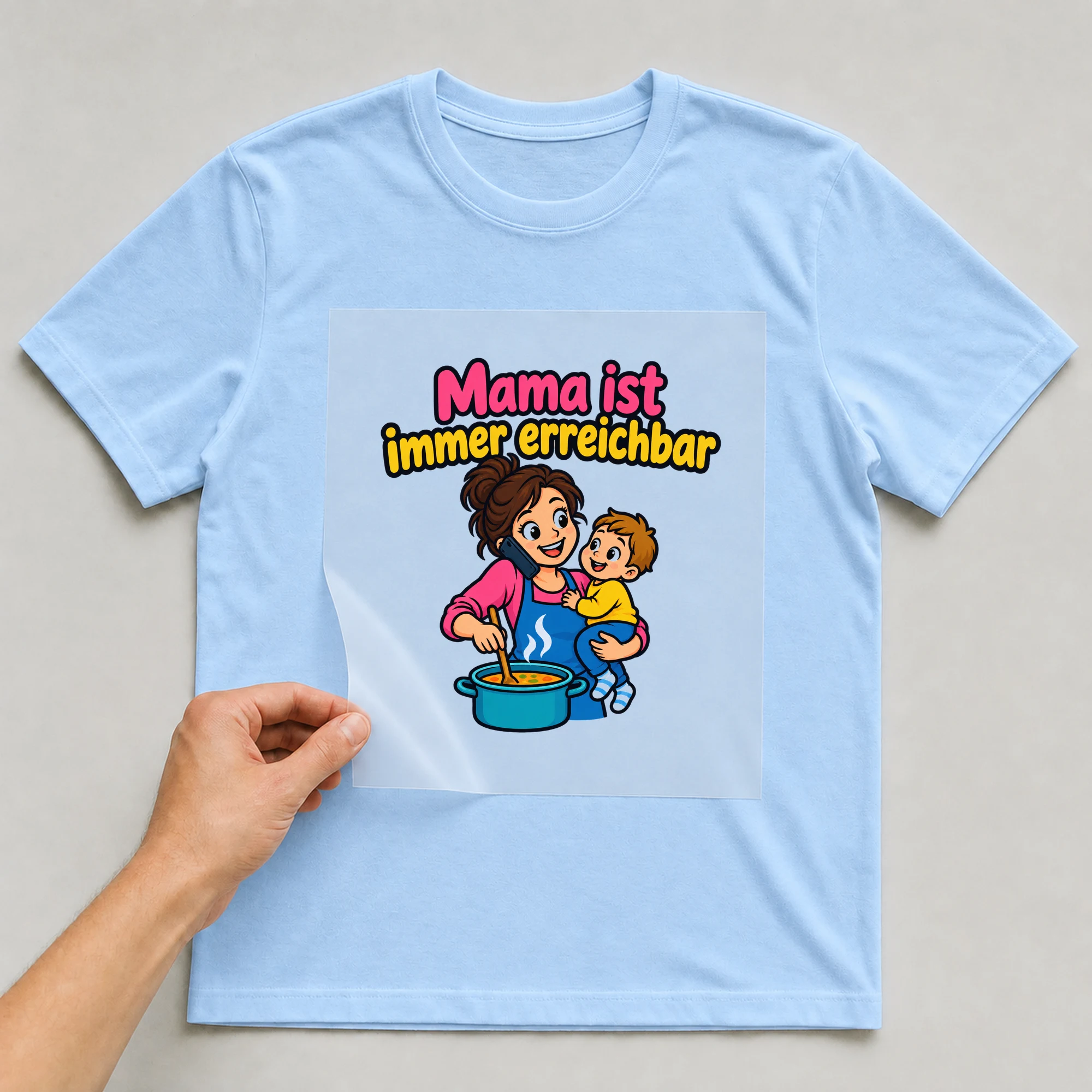 Bügelbild „Mama ist immer erreichbar“ auf babyblauem T-Shirt, Folie wird aufgelegt
