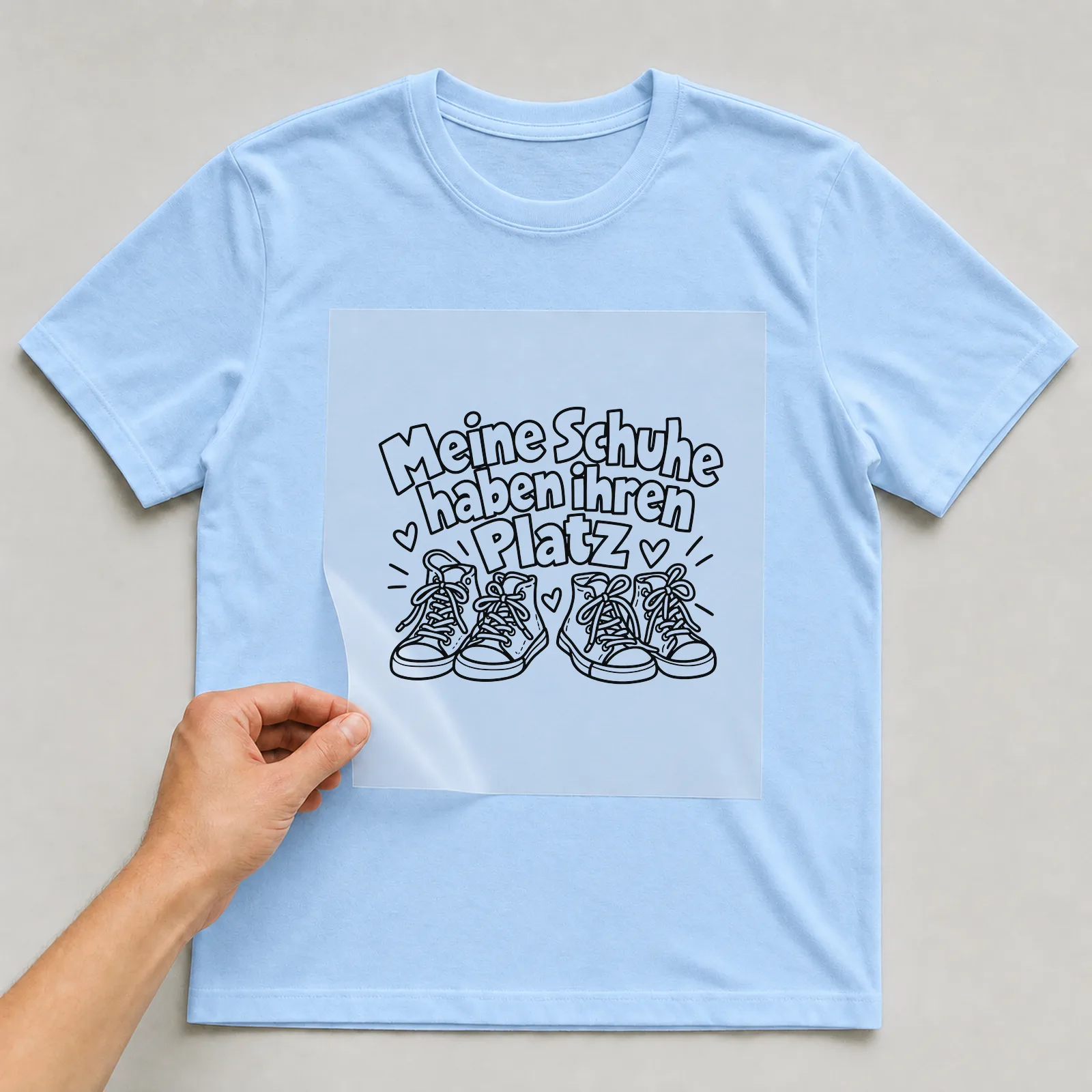 Bügelbild „Meine Schuhe haben ihren Platz“ auf hellblauem T-Shirt, Folie wird aufgelegt