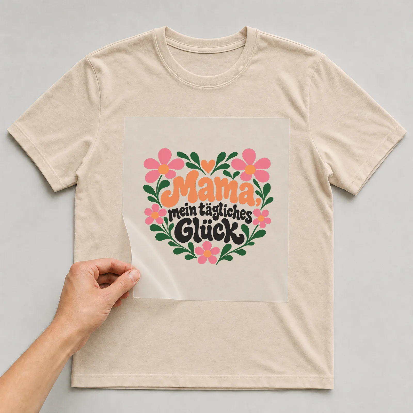 Bügelbild „Mama, mein tägliches Glück“ auf beigem T-Shirt, Folie wird aufgelegt