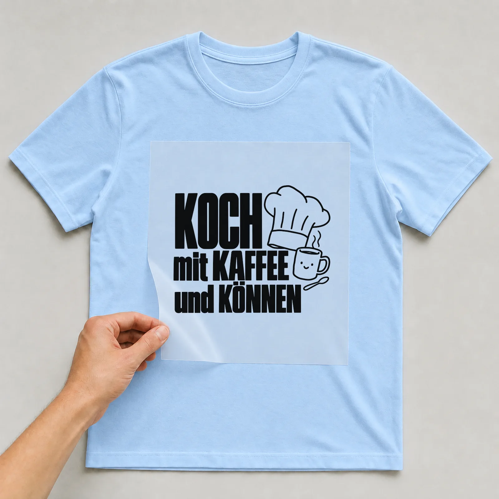Bügelbild „Koch mit Kaffee und Können“ auf hellblauem T-Shirt, Folie wird aufgelegt