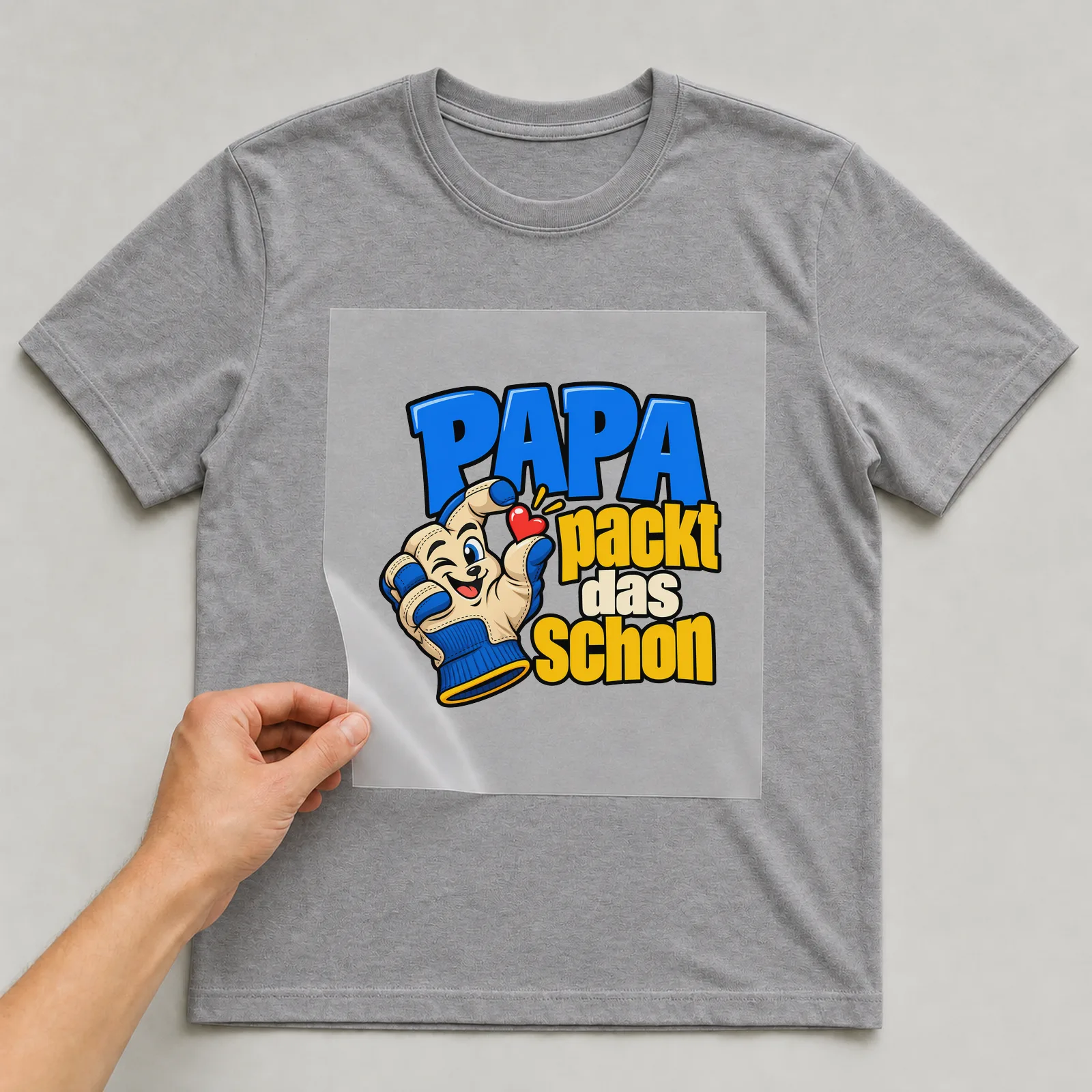 Bügelbild „Papa packt das schon“ auf grauem T-Shirt, Folie wird aufgelegt
