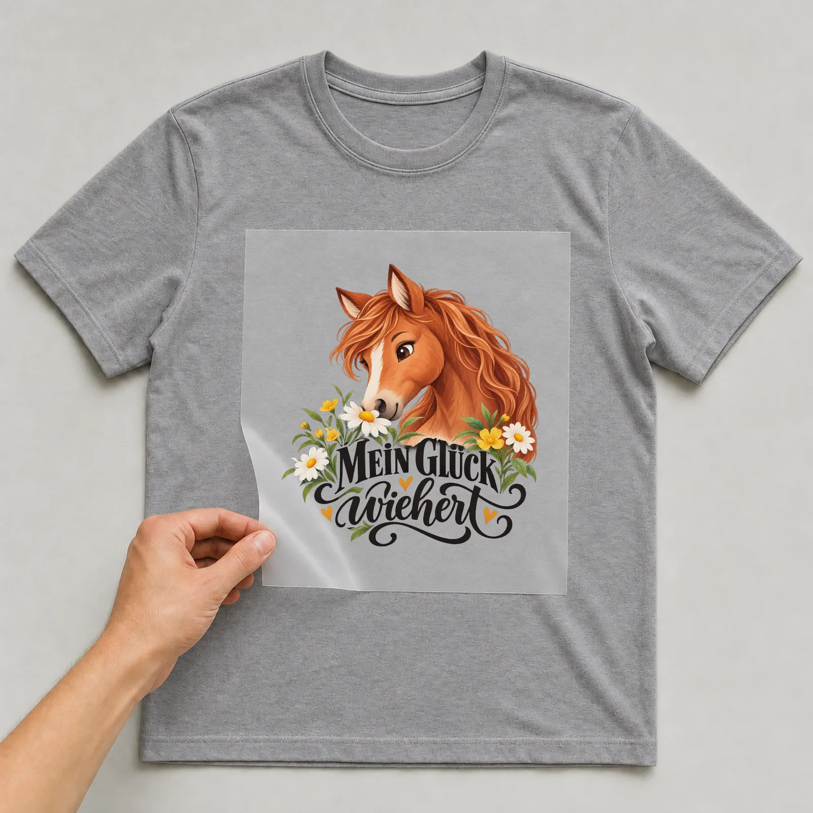 Bügelbild „Mein Glück wiehert“ auf grauem T-Shirt, Folie wird aufgelegt