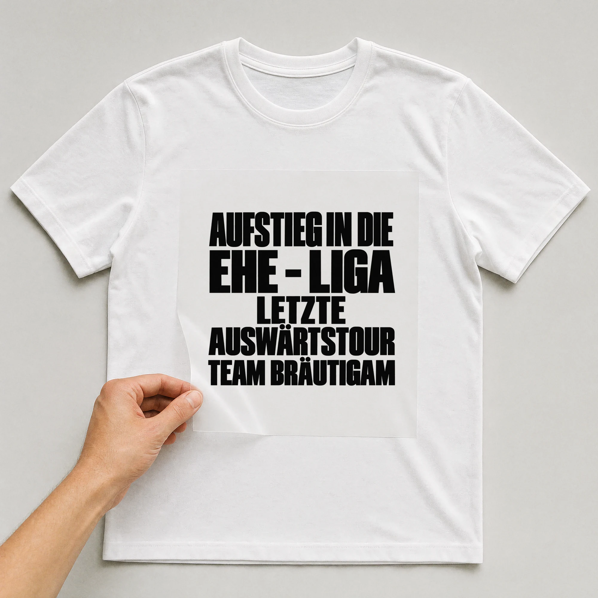 Bügelbild „Aufstieg in die Ehe - Liga letzte Auswärtstour Team Bräutigam“ auf weißem T-Shirt, Folie wird aufgelegt