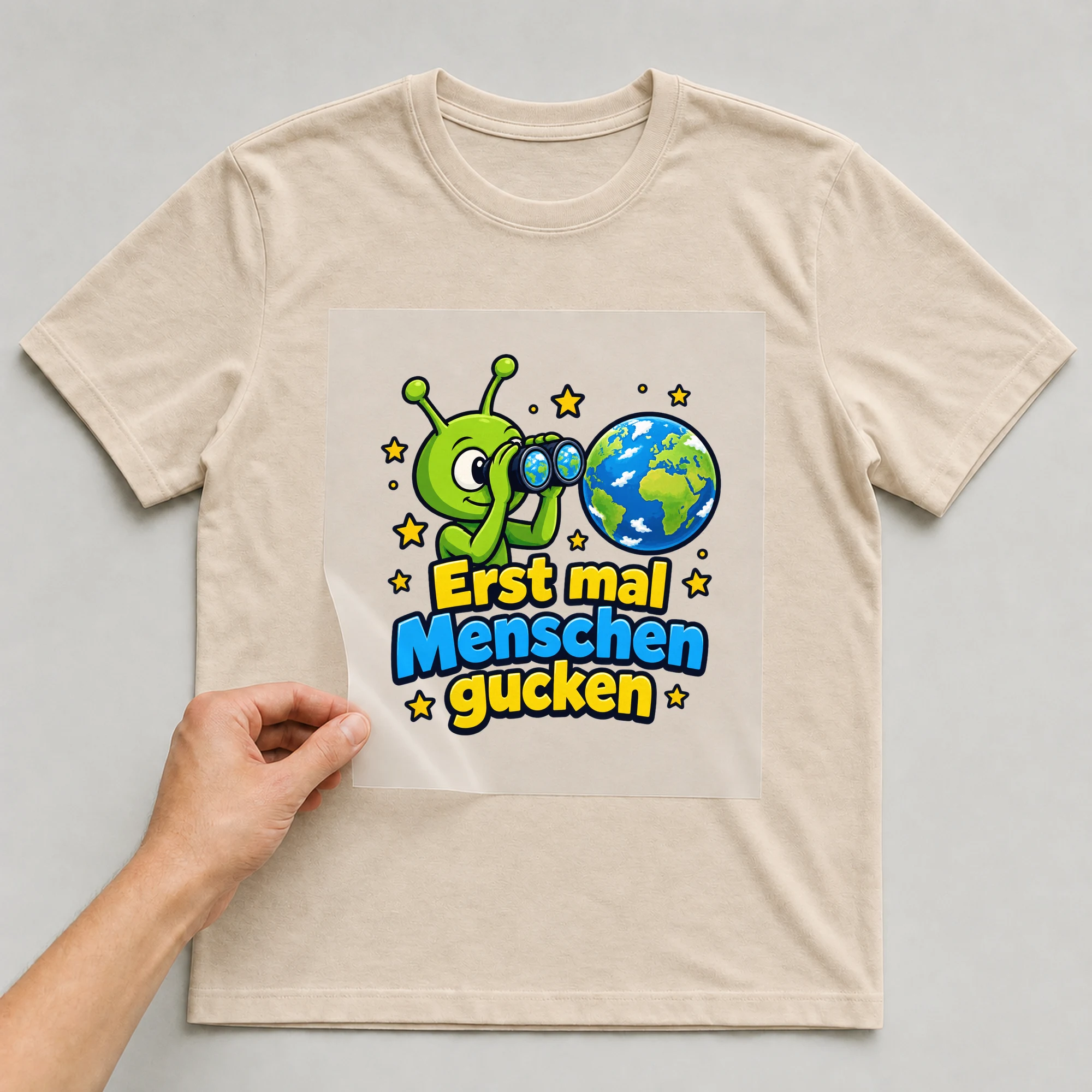 Bügelbild „Erst mal Menschen gucken“ auf beigem T-Shirt, Folie wird aufgelegt