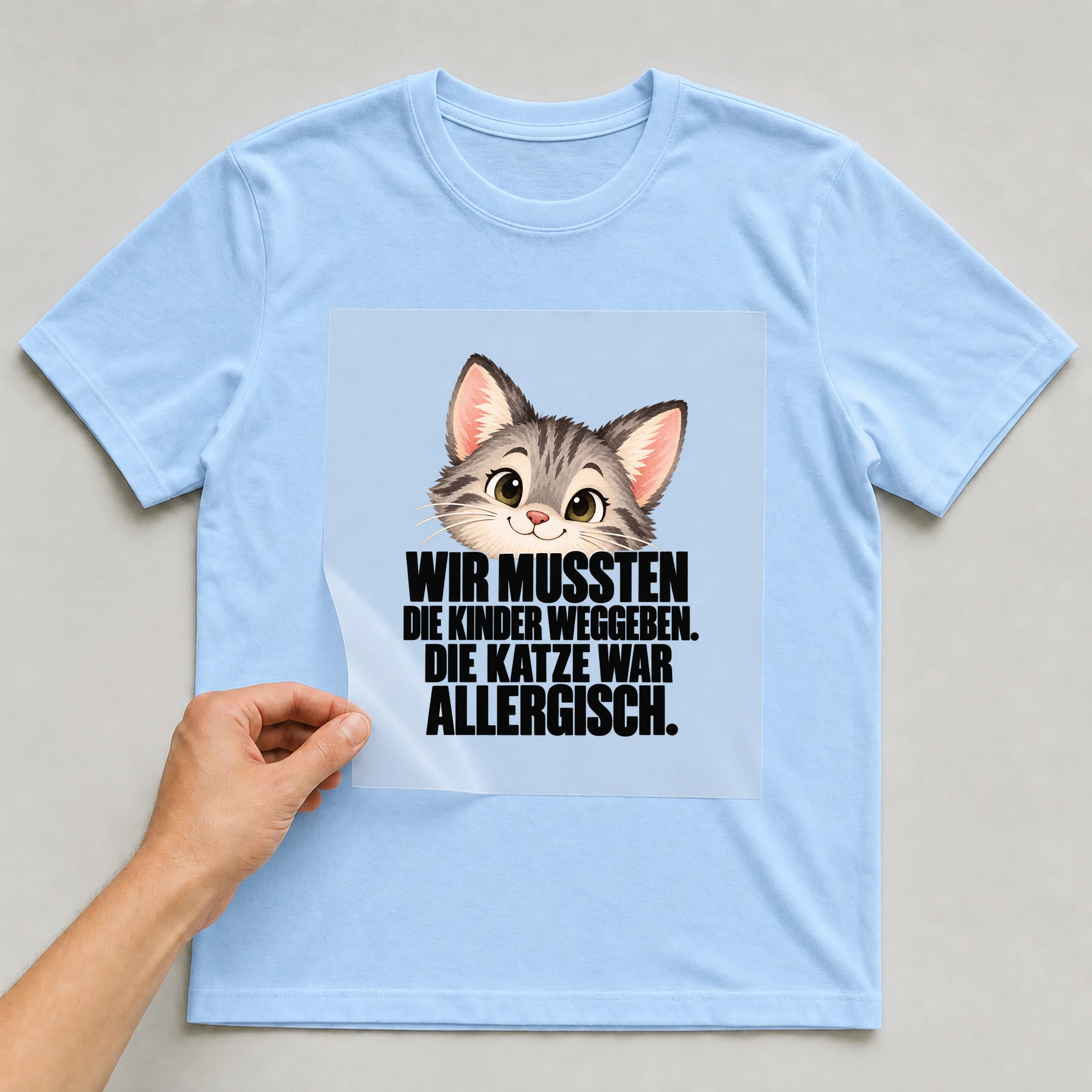 Bügelbild „Wir Mussten Die Kinder Weggeben. Die Katze War Allergisch.“ auf babyblauem T-Shirt, Folie wird aufgelegt