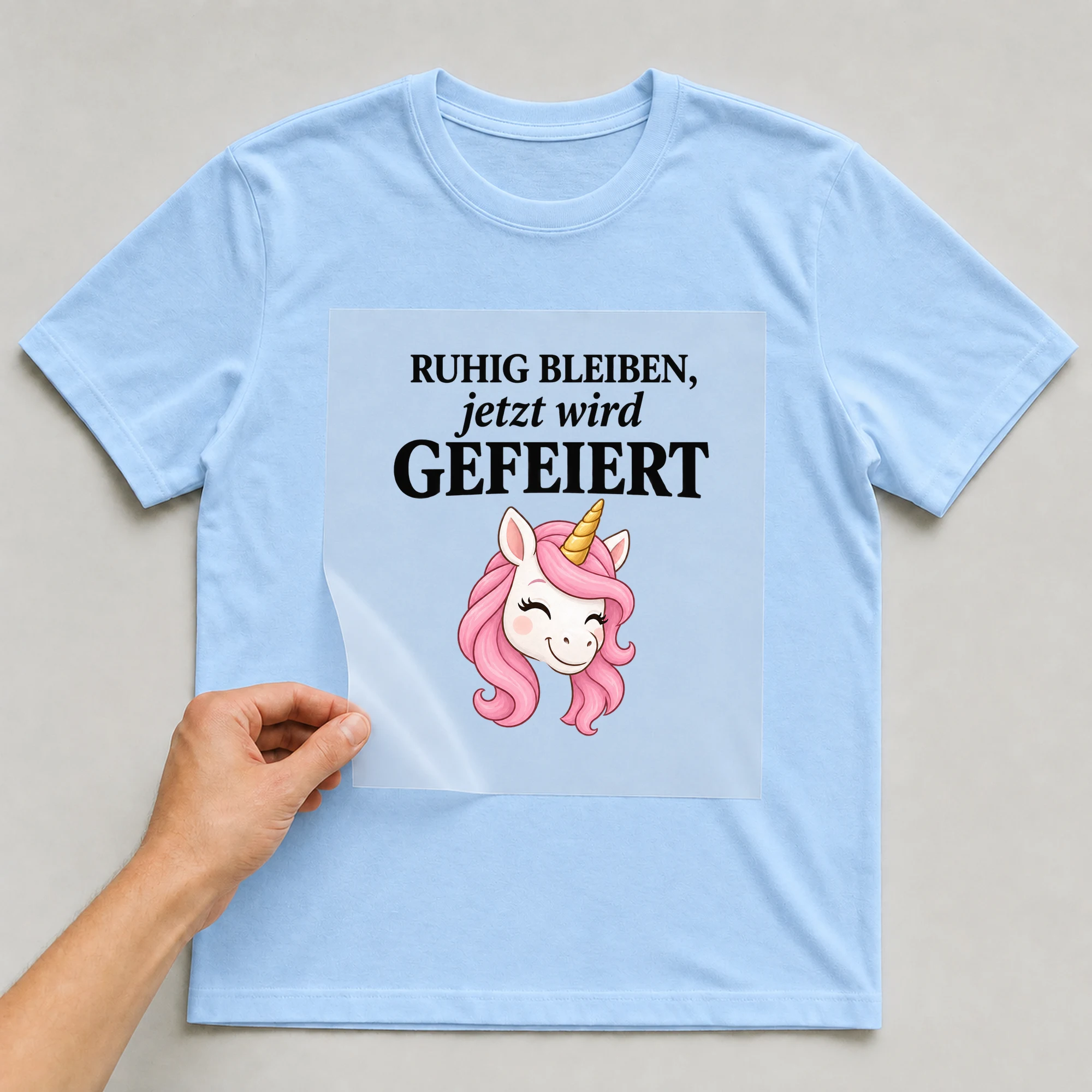 Bügelbild „Ruhig bleiben, jetzt wird gefeiert“ auf babyblauem T-Shirt, Folie wird aufgelegt