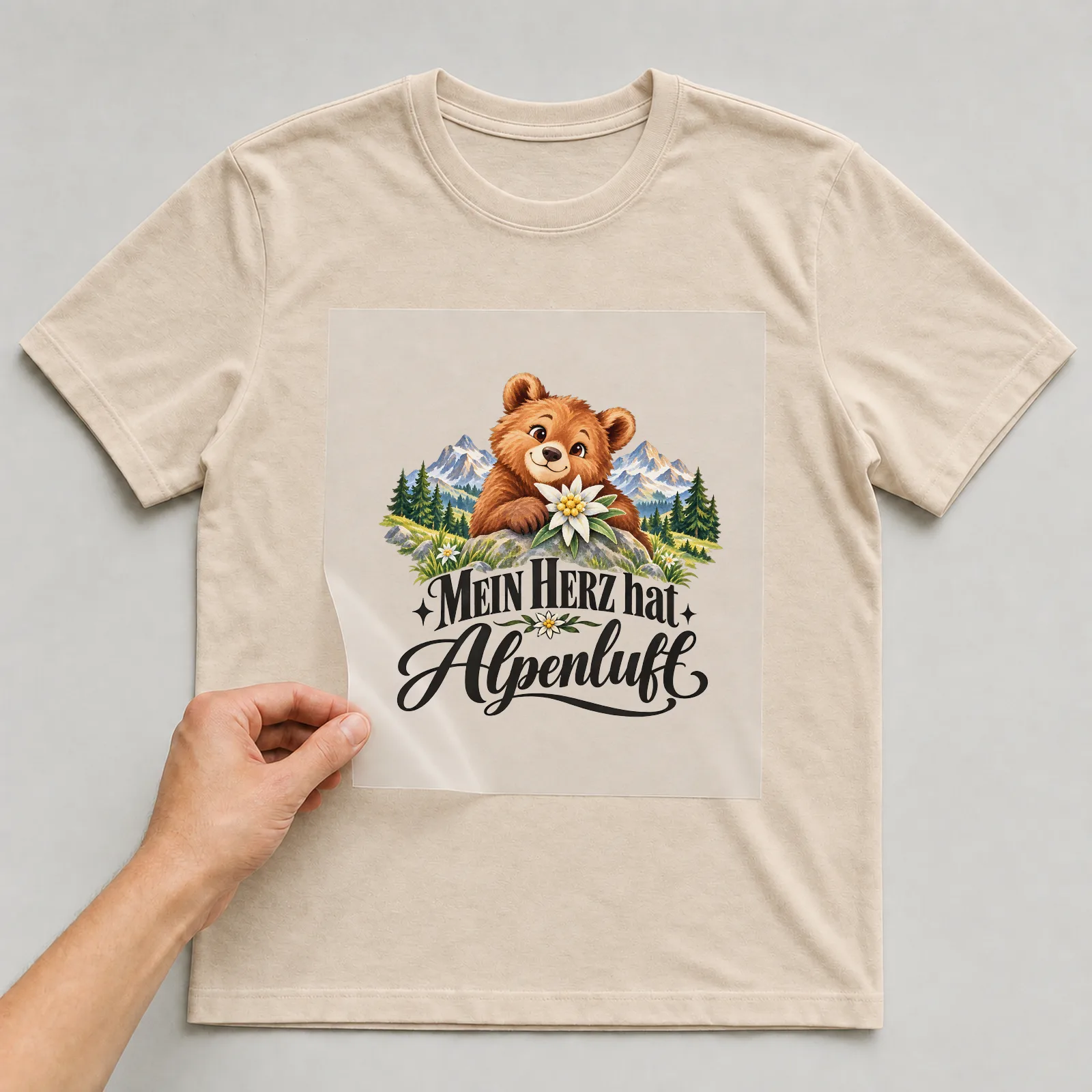 Bügelbild „Mein Herz hat Alpenluft“ auf beigem T-Shirt, Folie wird aufgelegt