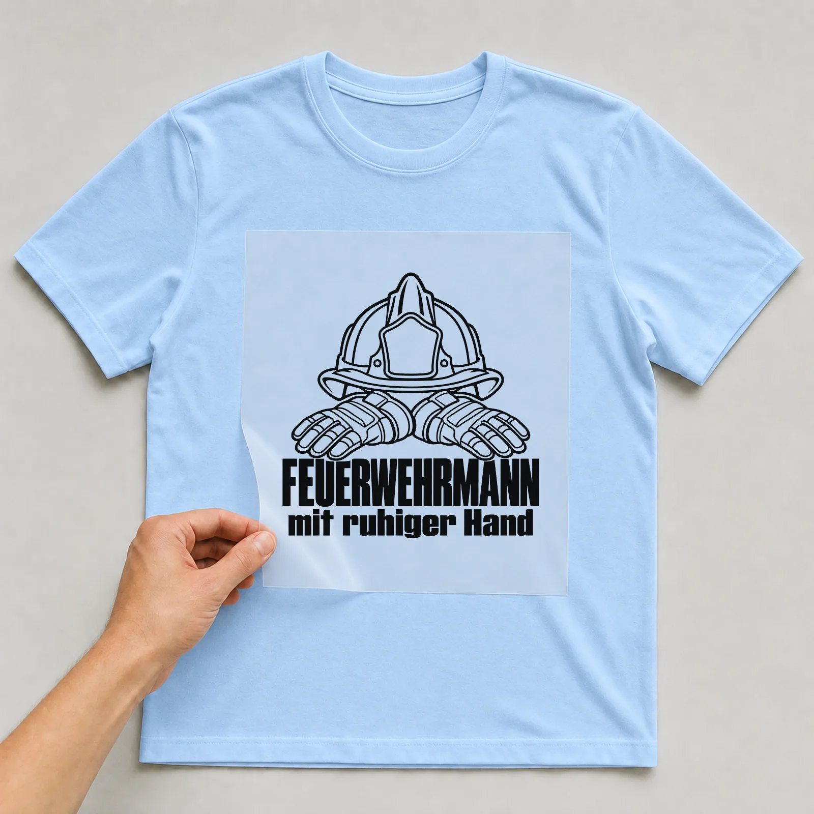 Bügelbild „Feuerwehrmann mit ruhiger Hand“ auf hellblauem T-Shirt, Folie wird aufgelegt