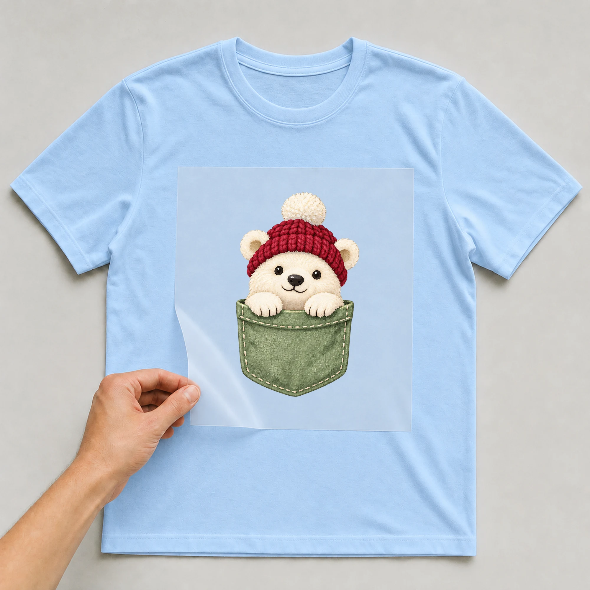 Bügelbild „Brusttasche Eisbär“ auf babyblauem T-Shirt, Folie wird aufgelegt