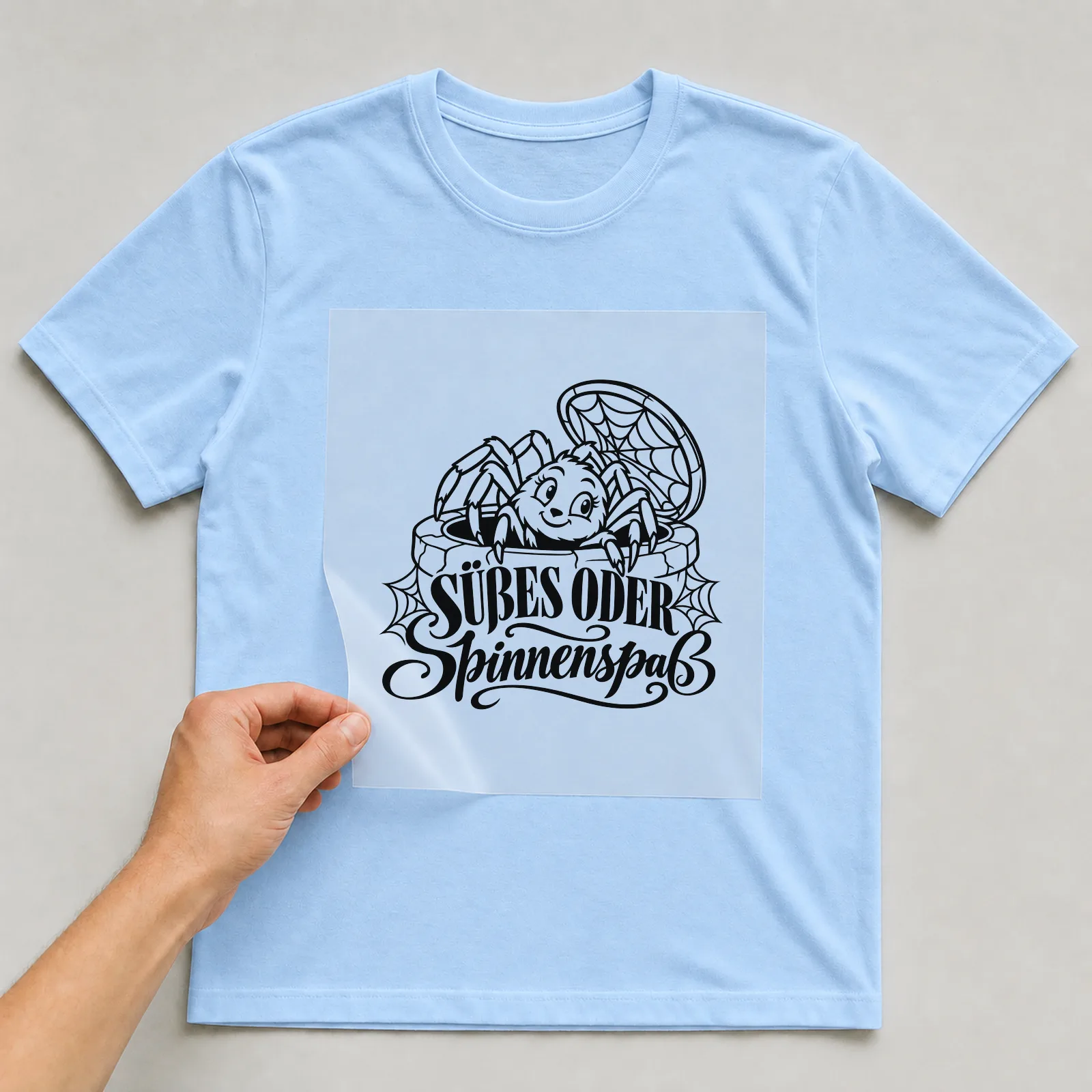 Bügelbild „Süßes oder Spinnenspaß“ auf hellblauem T-Shirt, Folie wird aufgelegt