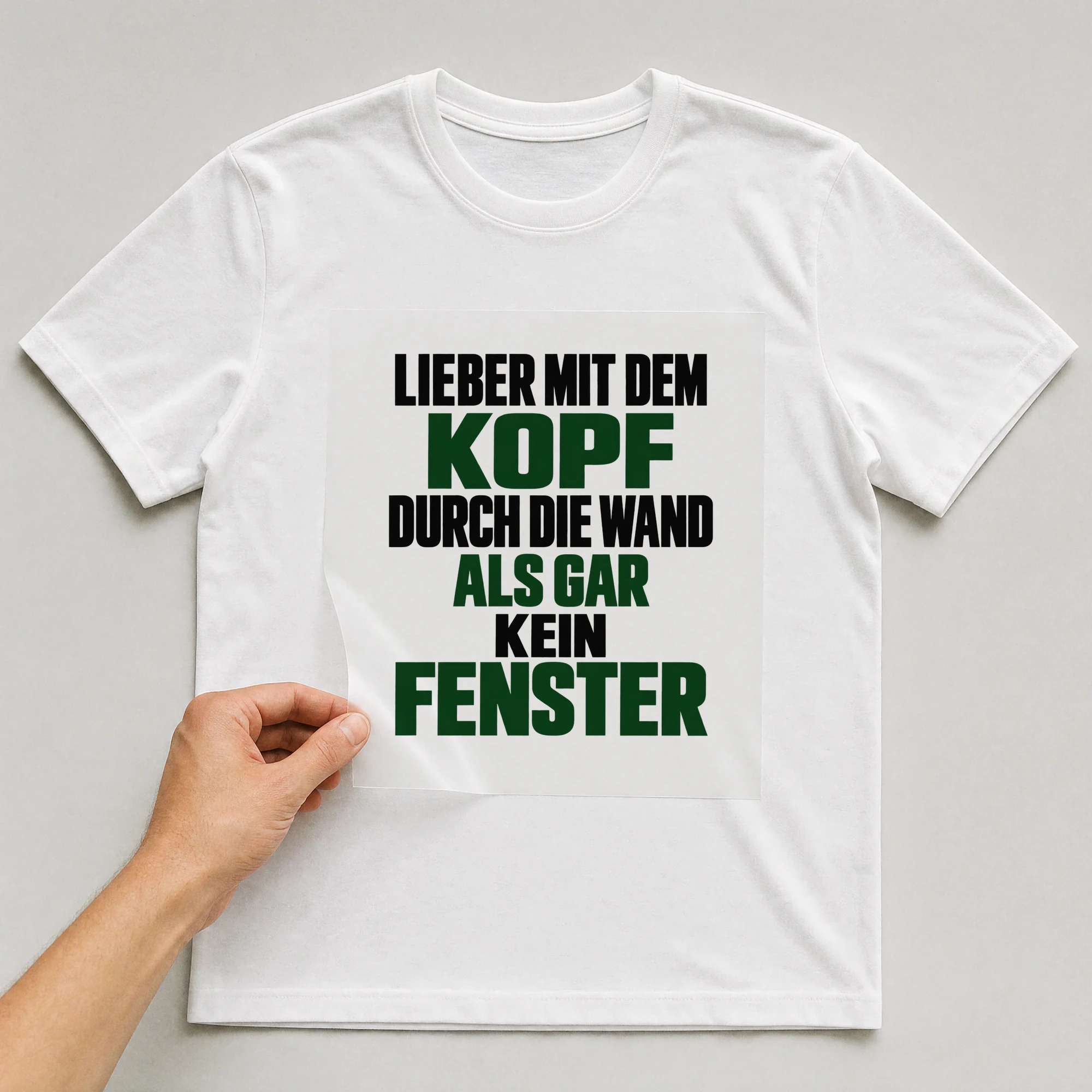 Bügelbild „Lieber mit dem Kopf durch die Wand als gar kein Fenster“ auf weißem T-Shirt, Folie wird aufgelegt