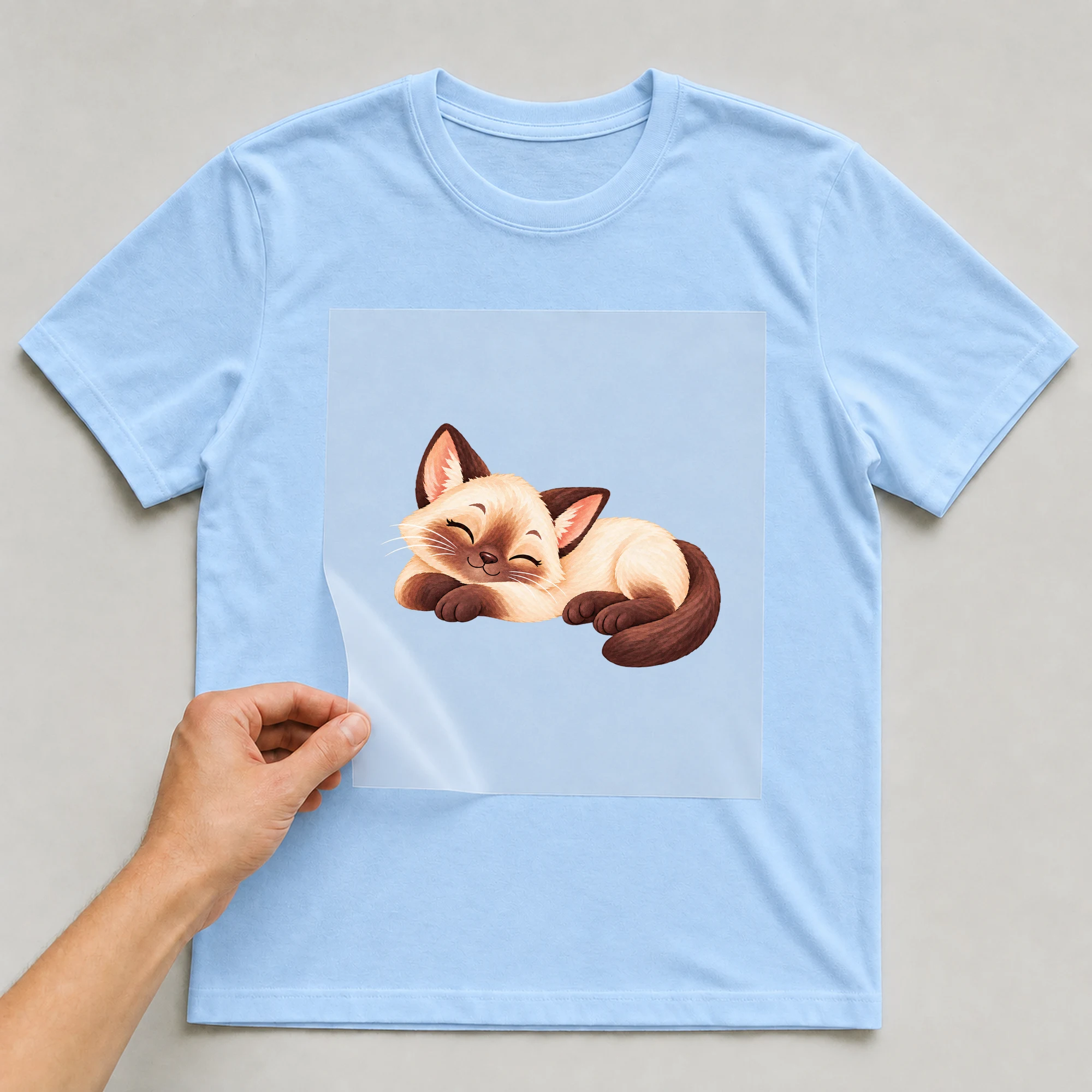 Bügelbild „Schlafende Katze“ auf babyblauem T-Shirt, Folie wird aufgelegt