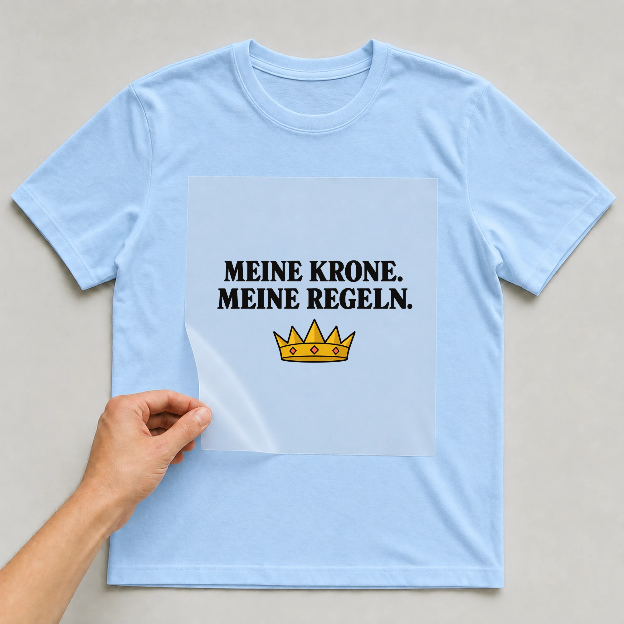Bügelbild „MEINE KRONE. MEINE REGELN.“ auf babyblauem T-Shirt, Folie wird aufgelegt