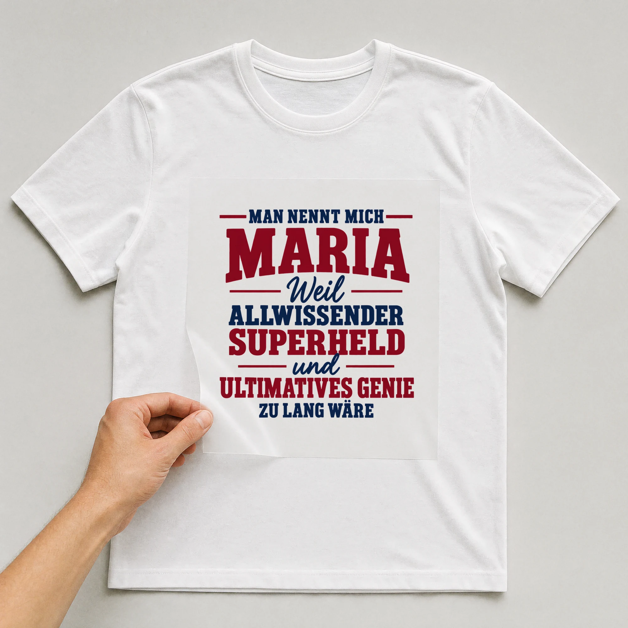 Bügelbild „Man nennt mich Maria weil allwissender Superheld und ultimatives Genie zu lang“ auf weißem T-Shirt, Folie wird aufgelegt