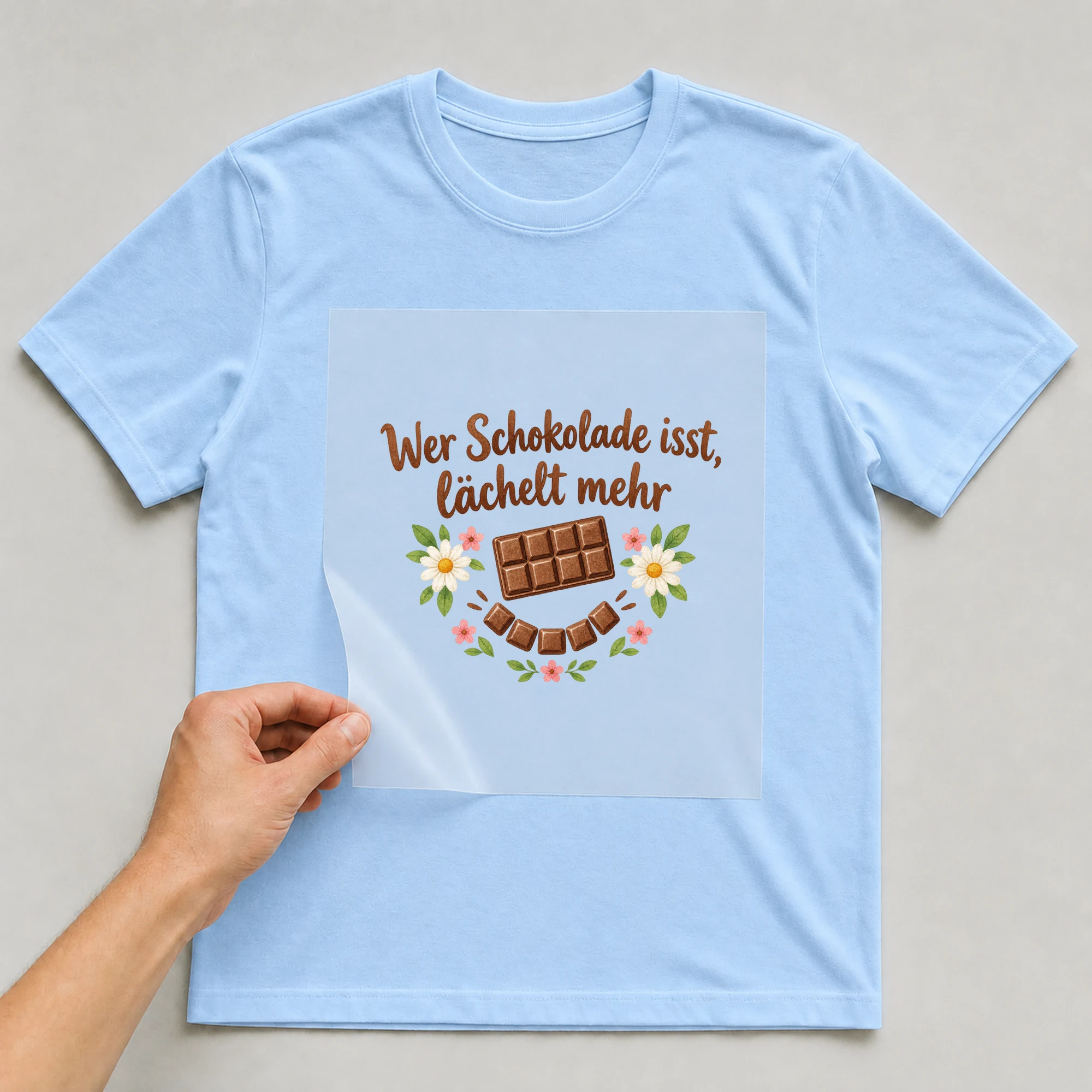 Bügelbild „Wer Schokolade isst, lächelt mehr“ auf babyblauem T-Shirt, Folie wird aufgelegt