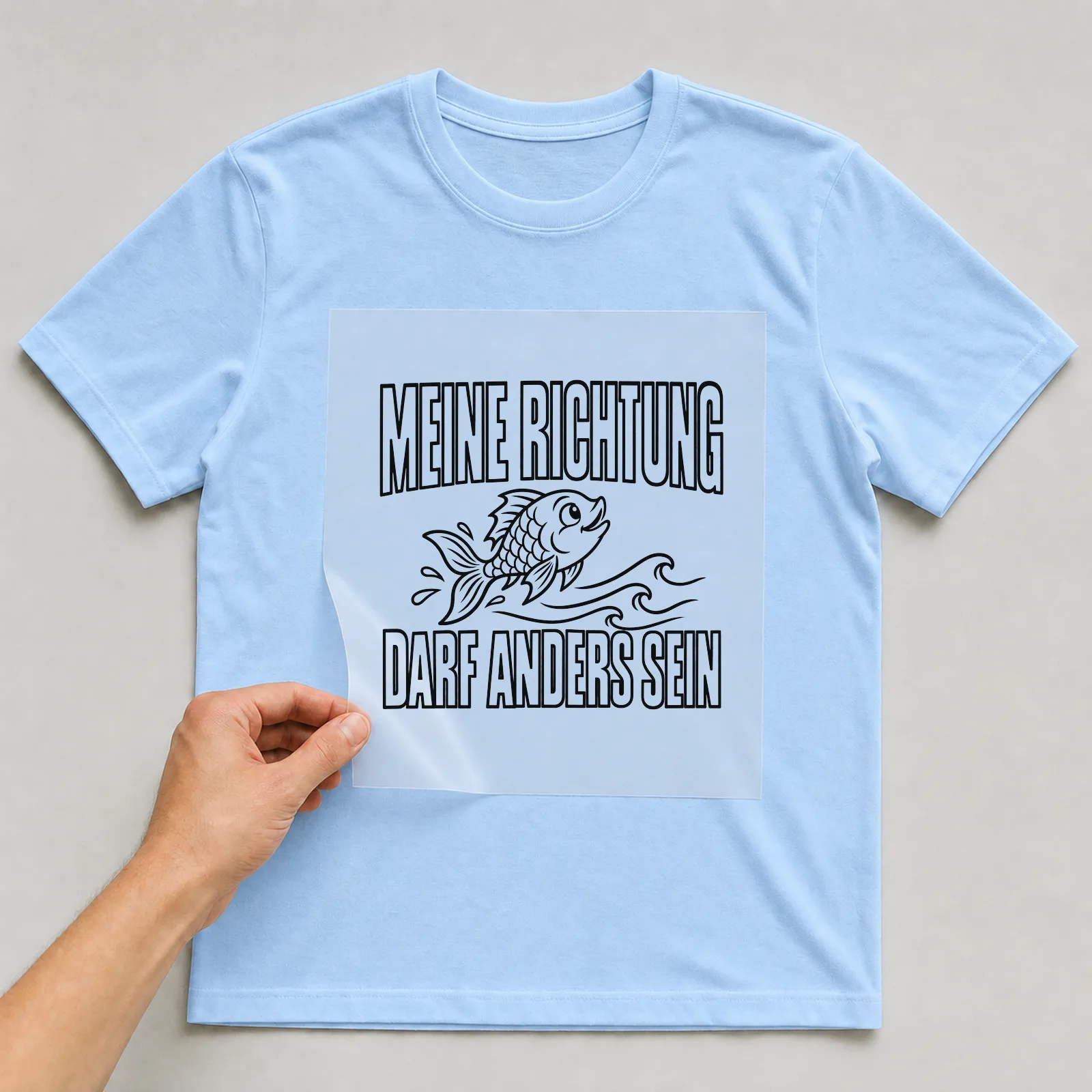 Bügelbild „Meine Richtung darf anders sein“ auf hellblauem T-Shirt, Folie wird aufgelegt